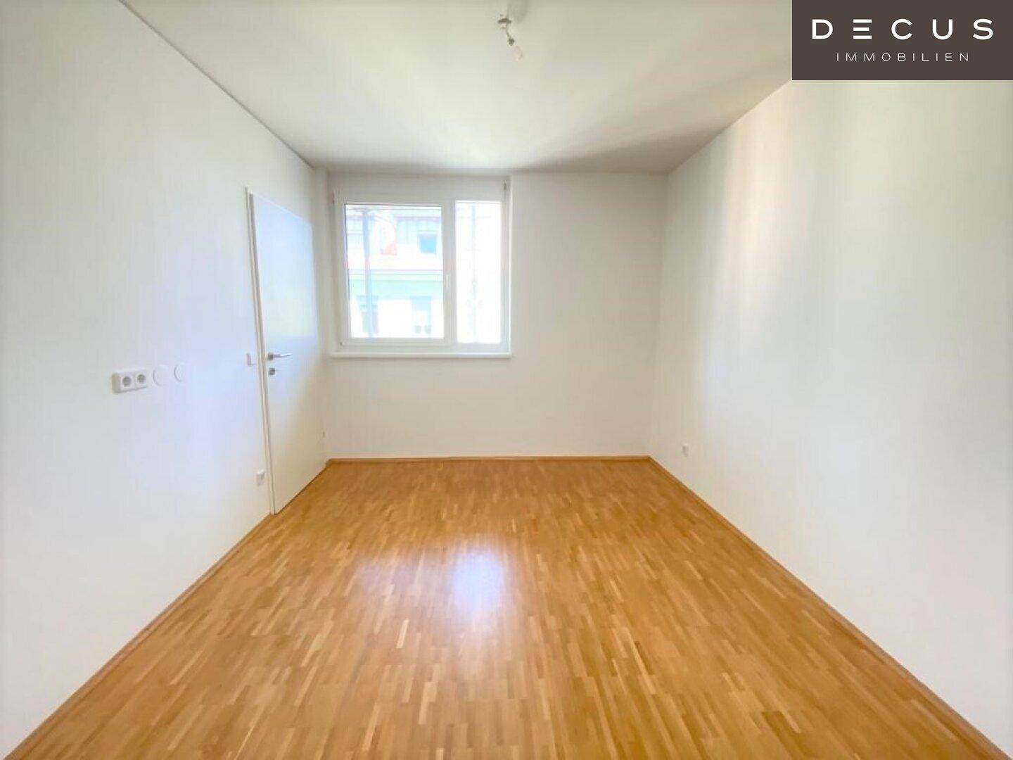 Leeres Schlafzimmer mit Parkettboden, weißen Wänden und einem Fenster für natürliches Licht.