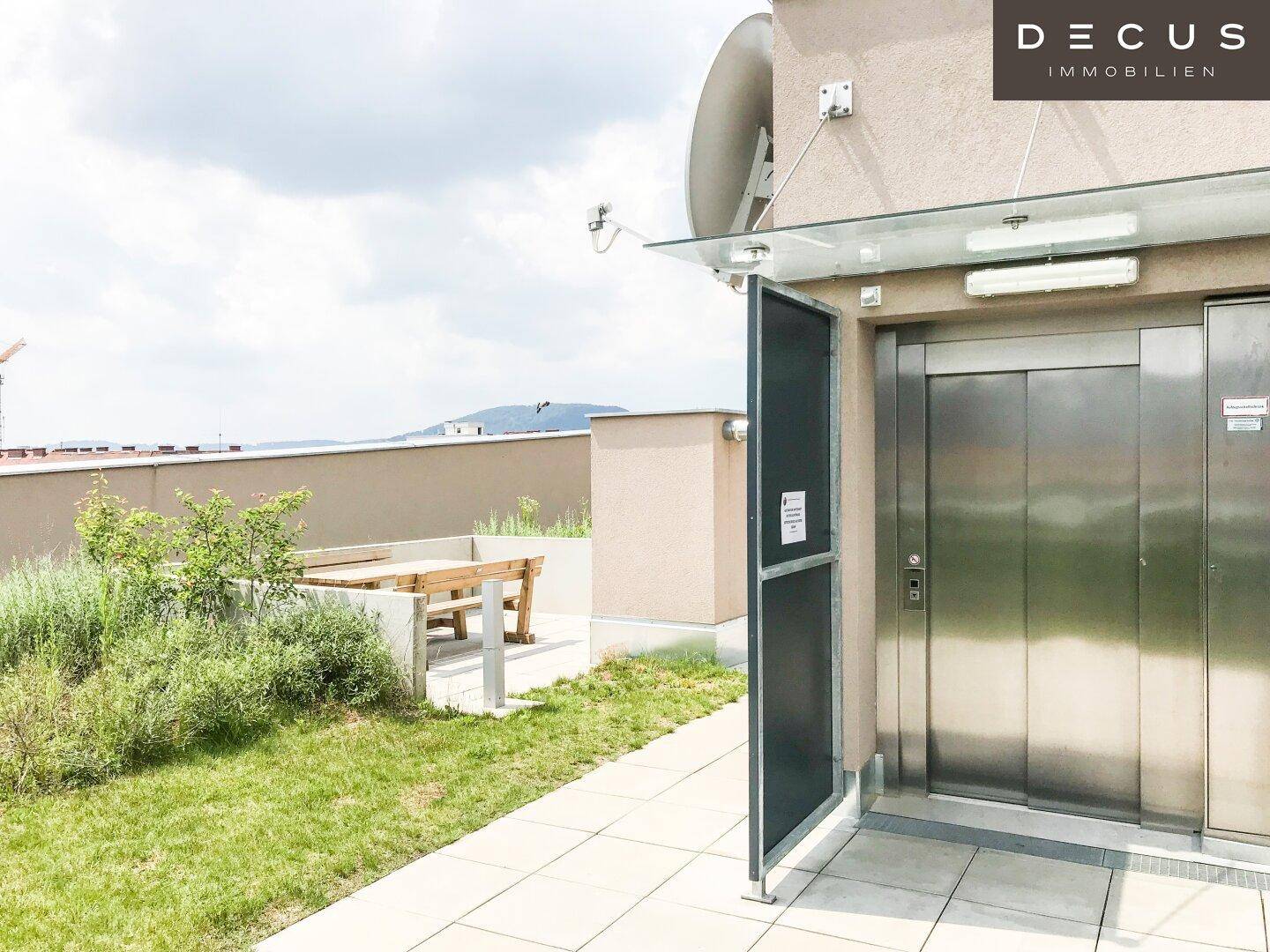 Dachterrasse mit direktem Aufzugzugang, Sitzgelegenheiten und grüner Bepflanzung, ideal für Entspannung.