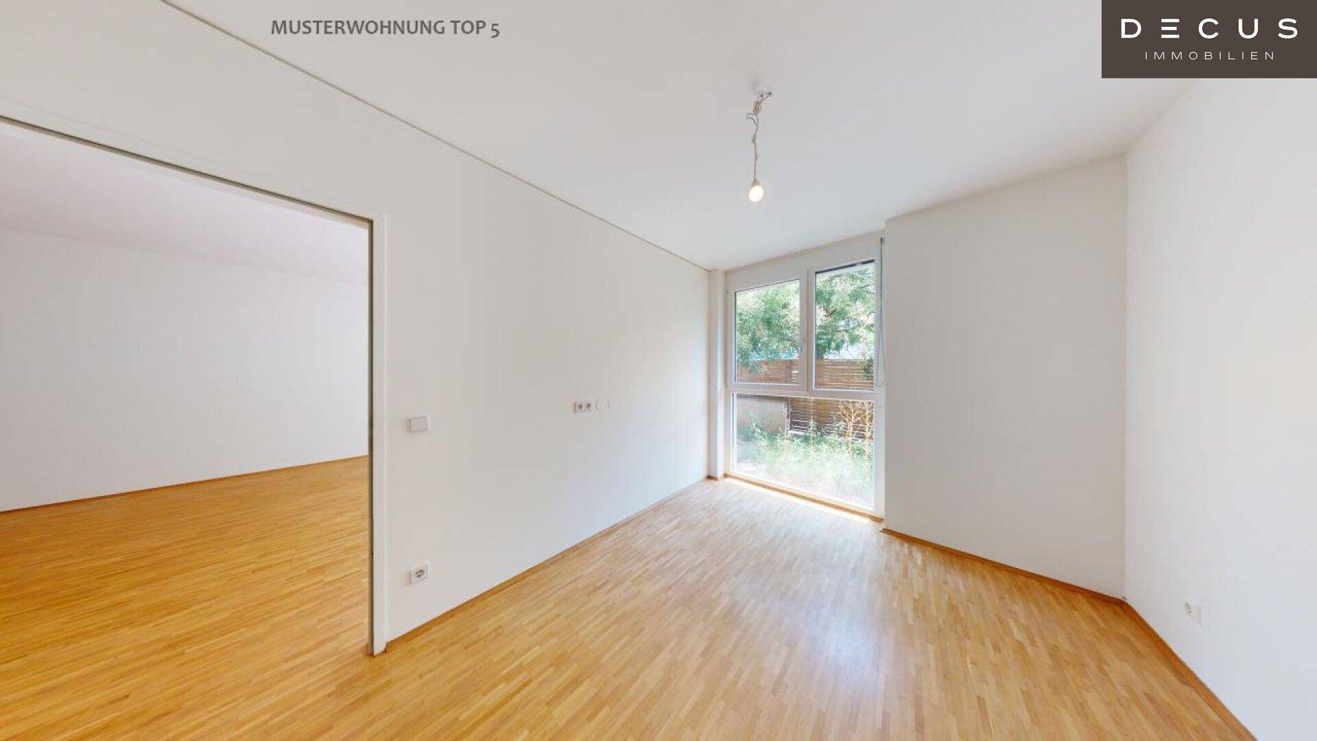 Lichtdurchflutetes Zimmer mit Parkettboden und Blick ins Grüne durch große Fenster.