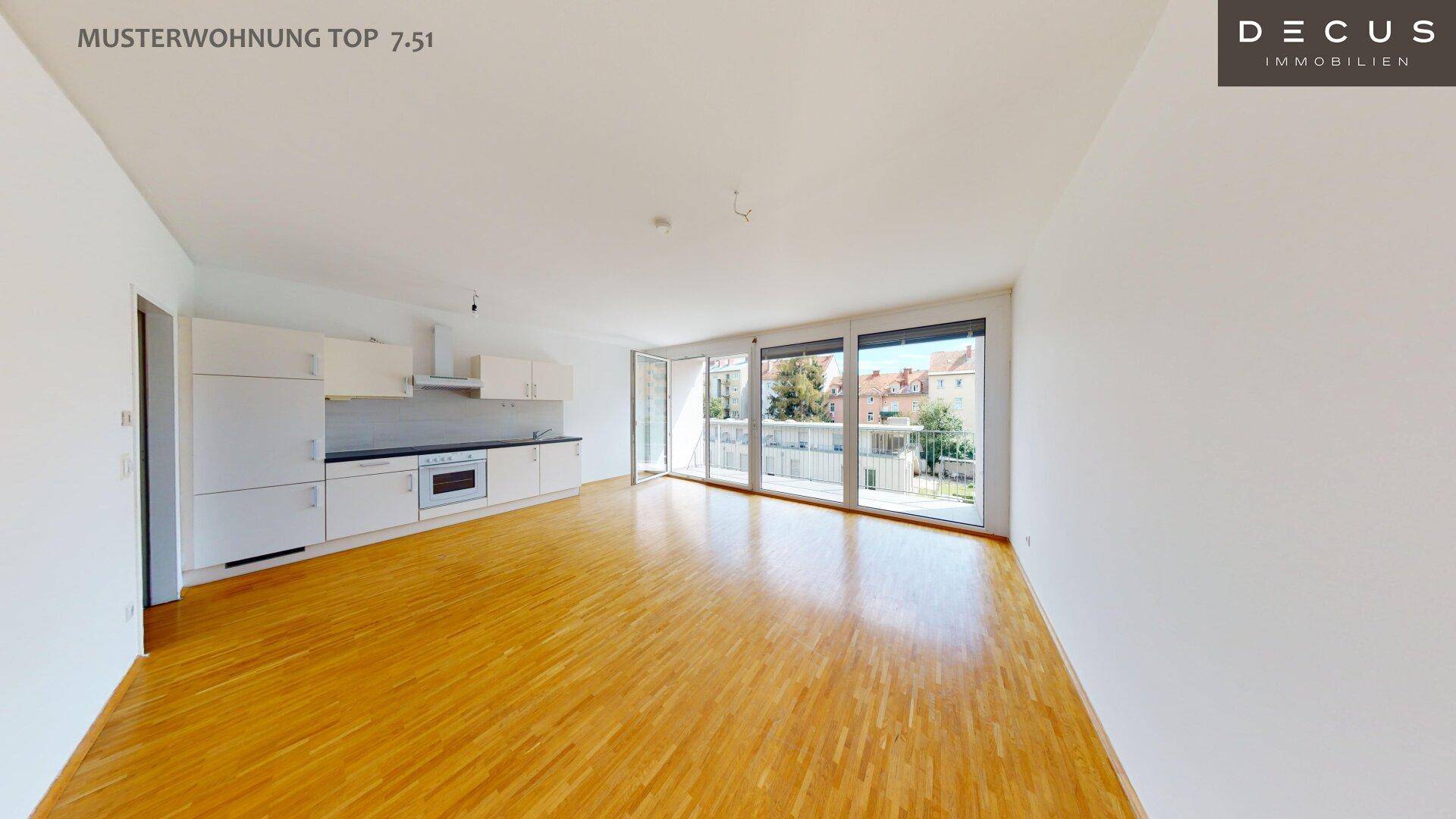 Geräumiger offener Wohnbereich mit integrierter Küche, Holzboden und großen Fenstern zum Balkon.