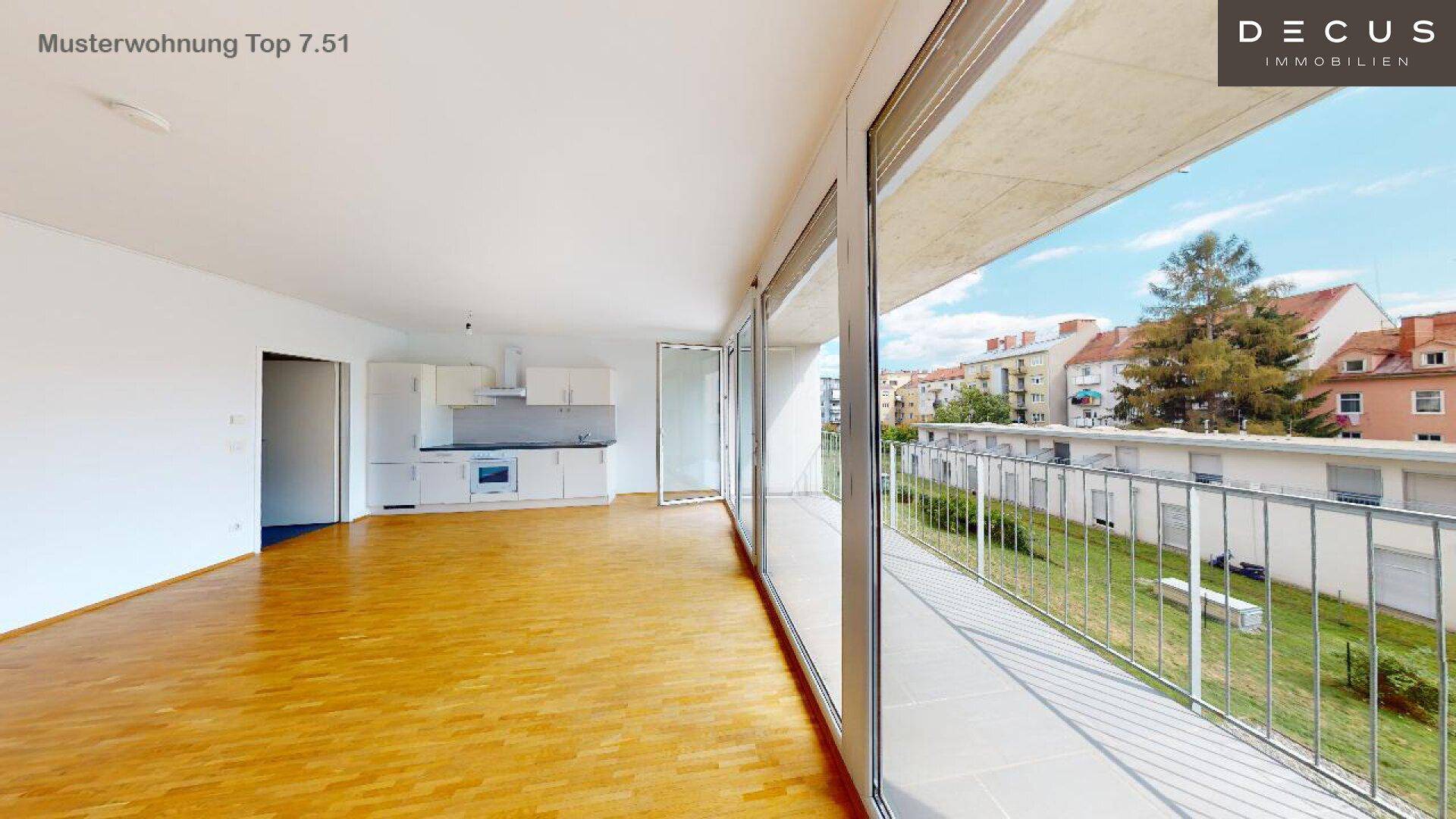 Heller offener Wohnbereich mit Holzboden, integrierter Küche und Zugang zu einem großen Balkon.