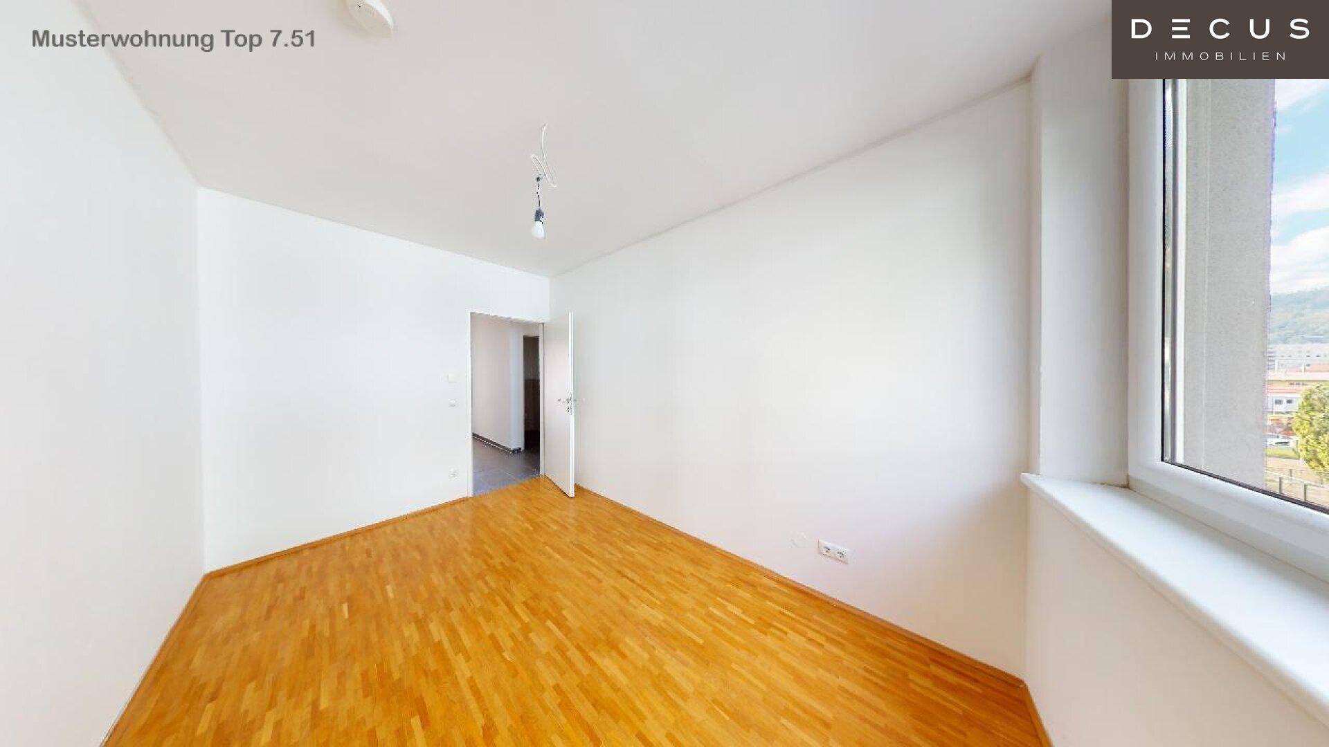 Helles Schlafzimmer mit Holzboden und großen Fenstern, die viel Tageslicht hereinlassen.