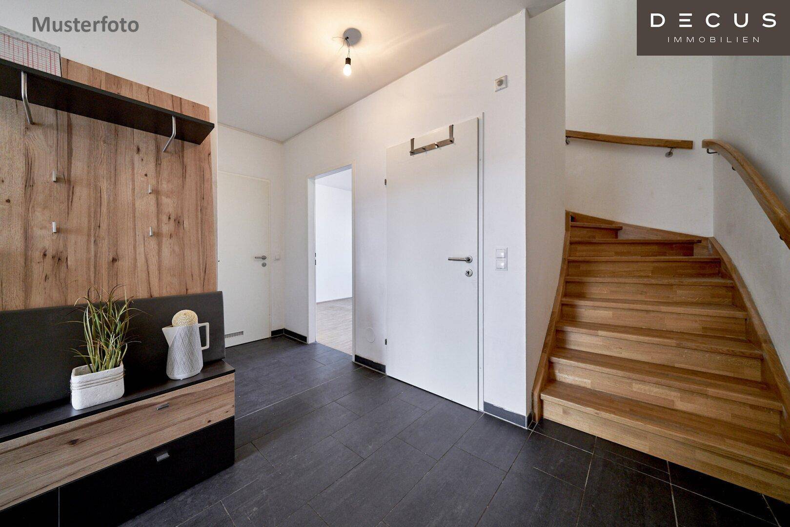 Eingangsbereich mit dunklem Fliesenboden, Garderobe und Holztreppe zu den oberen Etagen.