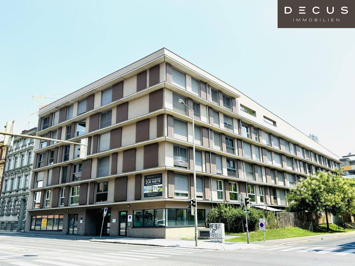 Modernes Mehrfamilienhaus an einer Straßenecke mit vielen Fenstern und Balkonen.