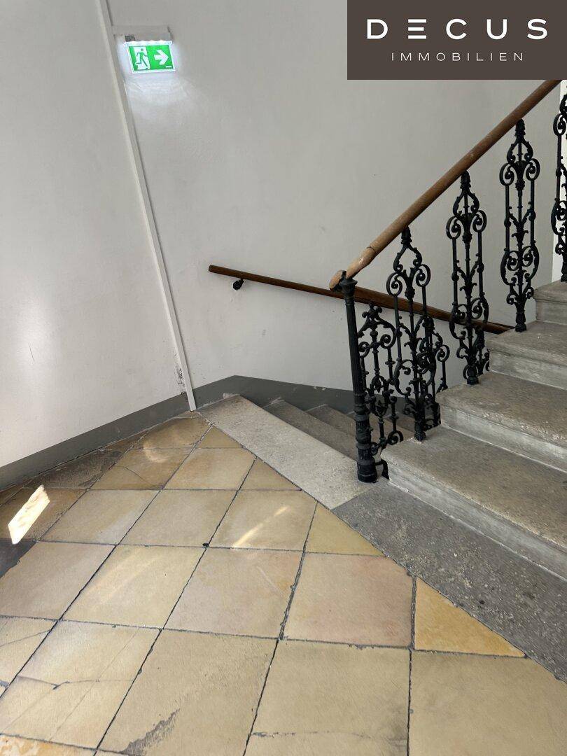 Historisches Treppenhaus mit kunstvollem schmiedeeisernem Geländer, Holzhandlauf und gefliestem Boden.