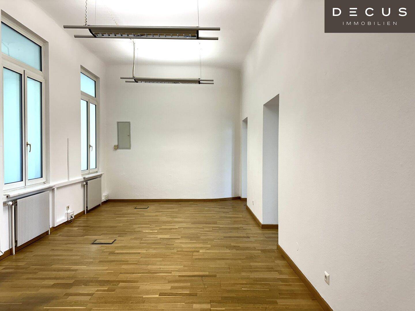 Langer Büroraum mit Holzboden und hohen Decken, ausgestattet mit modernen Deckenleuchten.