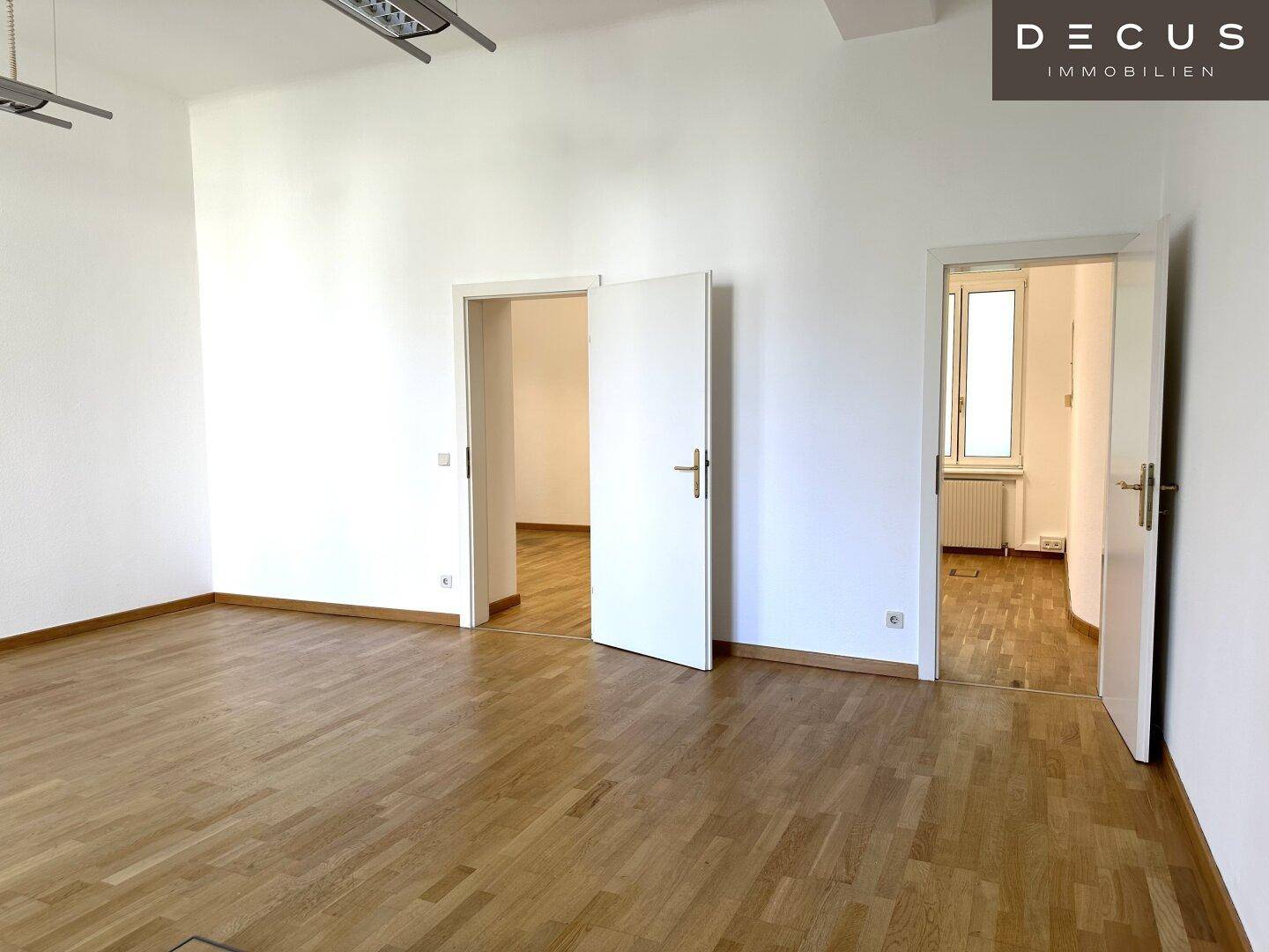 Geräumiger Büroraum mit Holzboden und mehreren Türen, die zu weiteren Räumen führen.