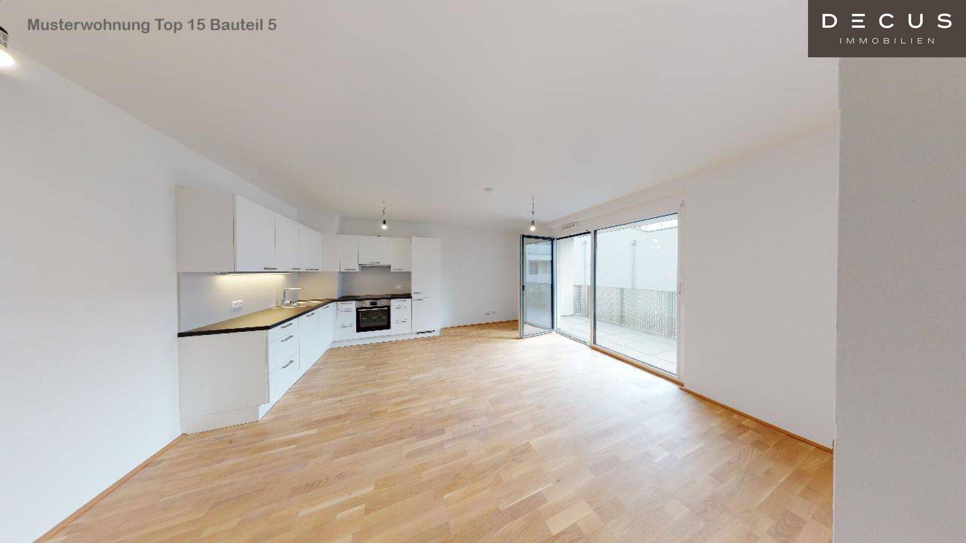 Offener Wohnbereich mit integrierter weißer Einbauküche, Holzboden und Zugang zur Terrasse.