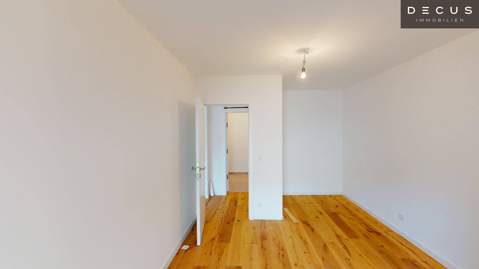Geräumiges, helles Zimmer mit Holzboden und offenem Durchgang zu einem weiteren Raum.