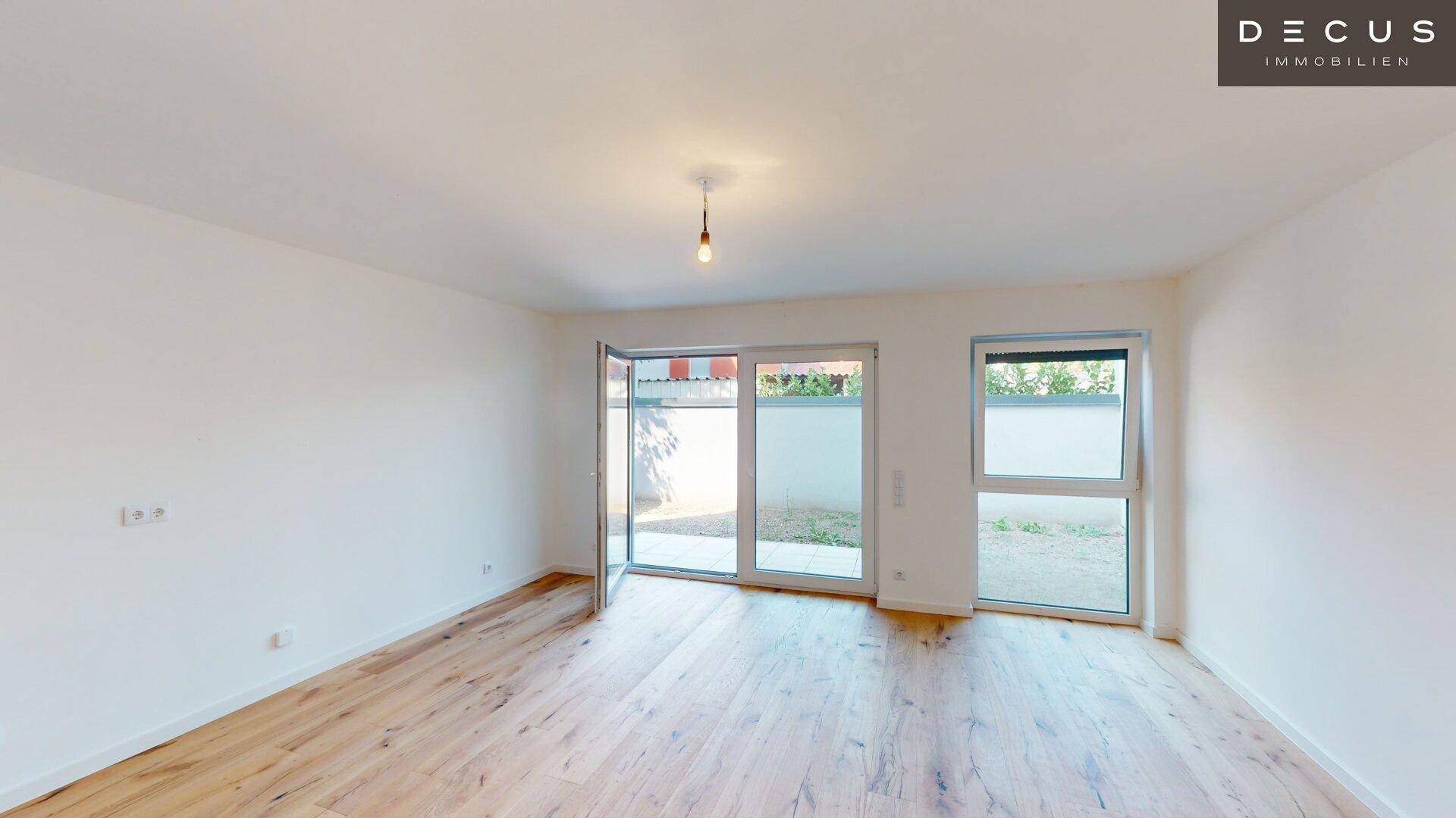 Lichtdurchflutetes Zimmer mit Holzboden und großen Fenstern, die den Blick nach draußen freigeben.