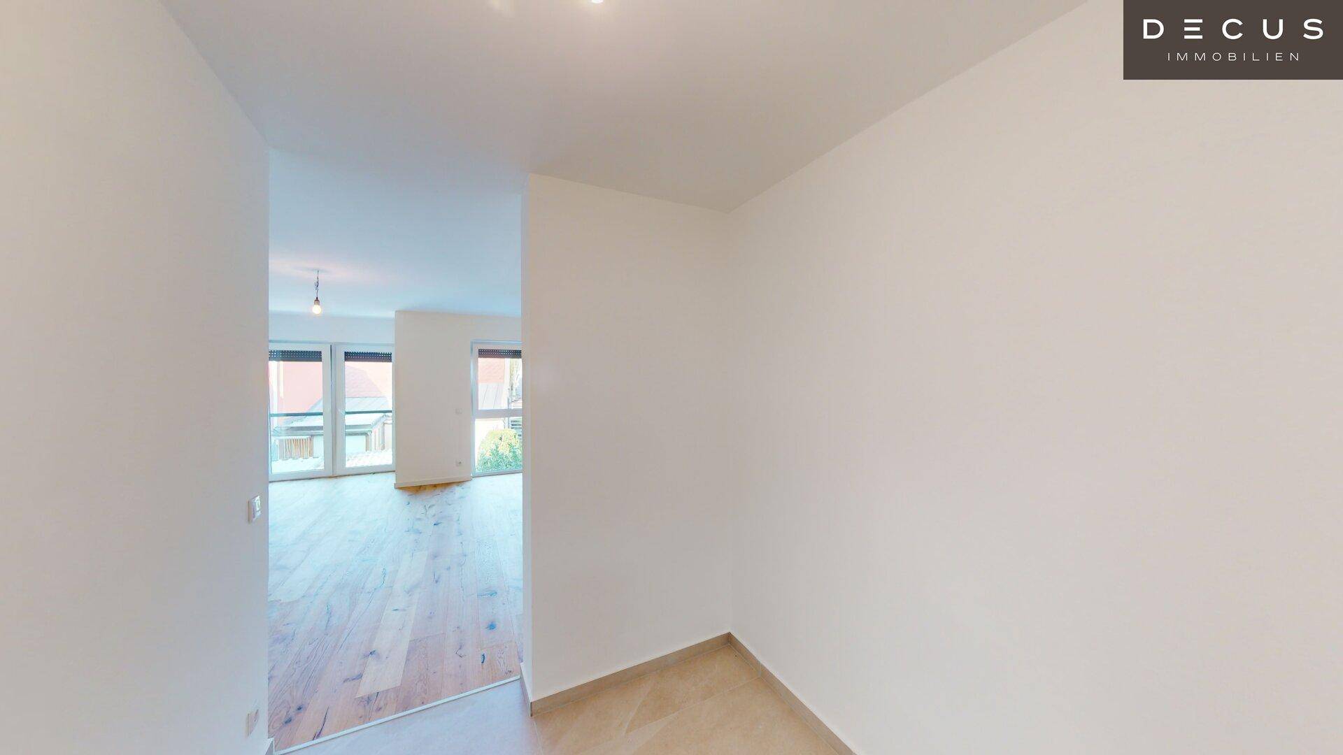 Heller Flur mit Fliesenboden, der in einen Wohnbereich mit Holzboden übergeht.