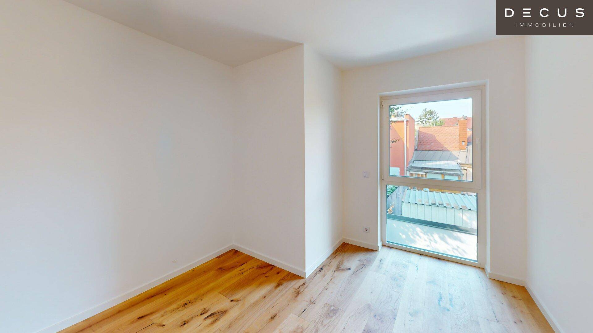 Heller Raum mit Holzboden und einem großen Fenster, das viel natürliches Licht spendet.
