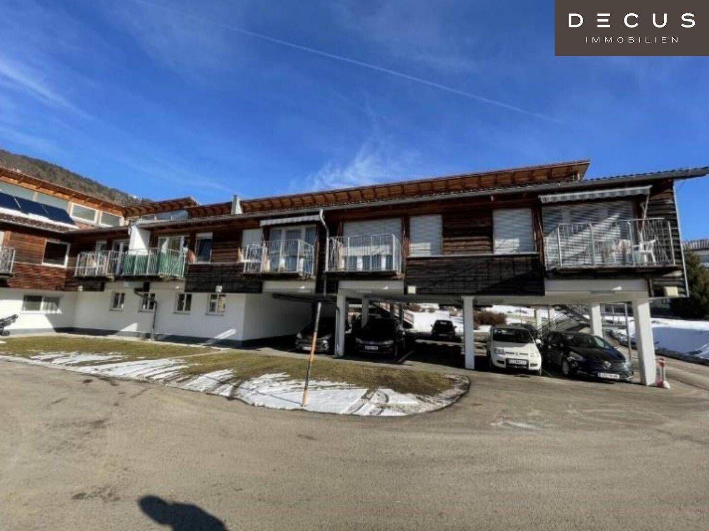 Moderner Gebäudekomplex mit Holzfassade, Balkonen und integrierten Carports im Winter.