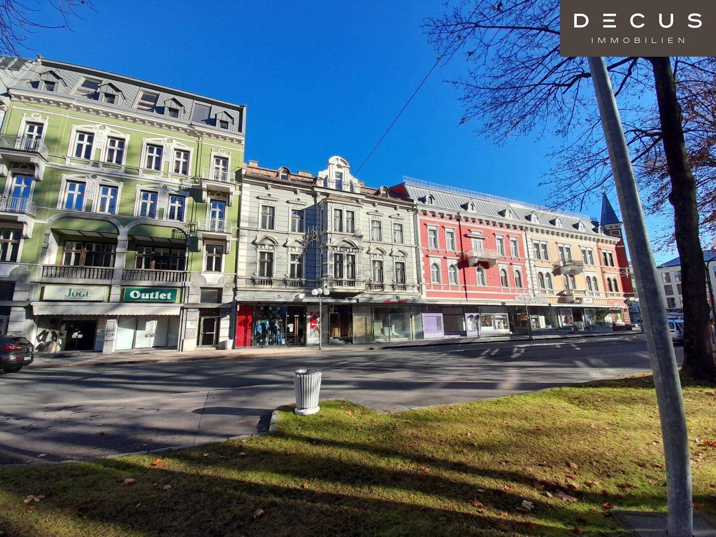 Historische Gebäudezeile mit Geschäften und Wohnungen entlang einer sonnigen Straße.