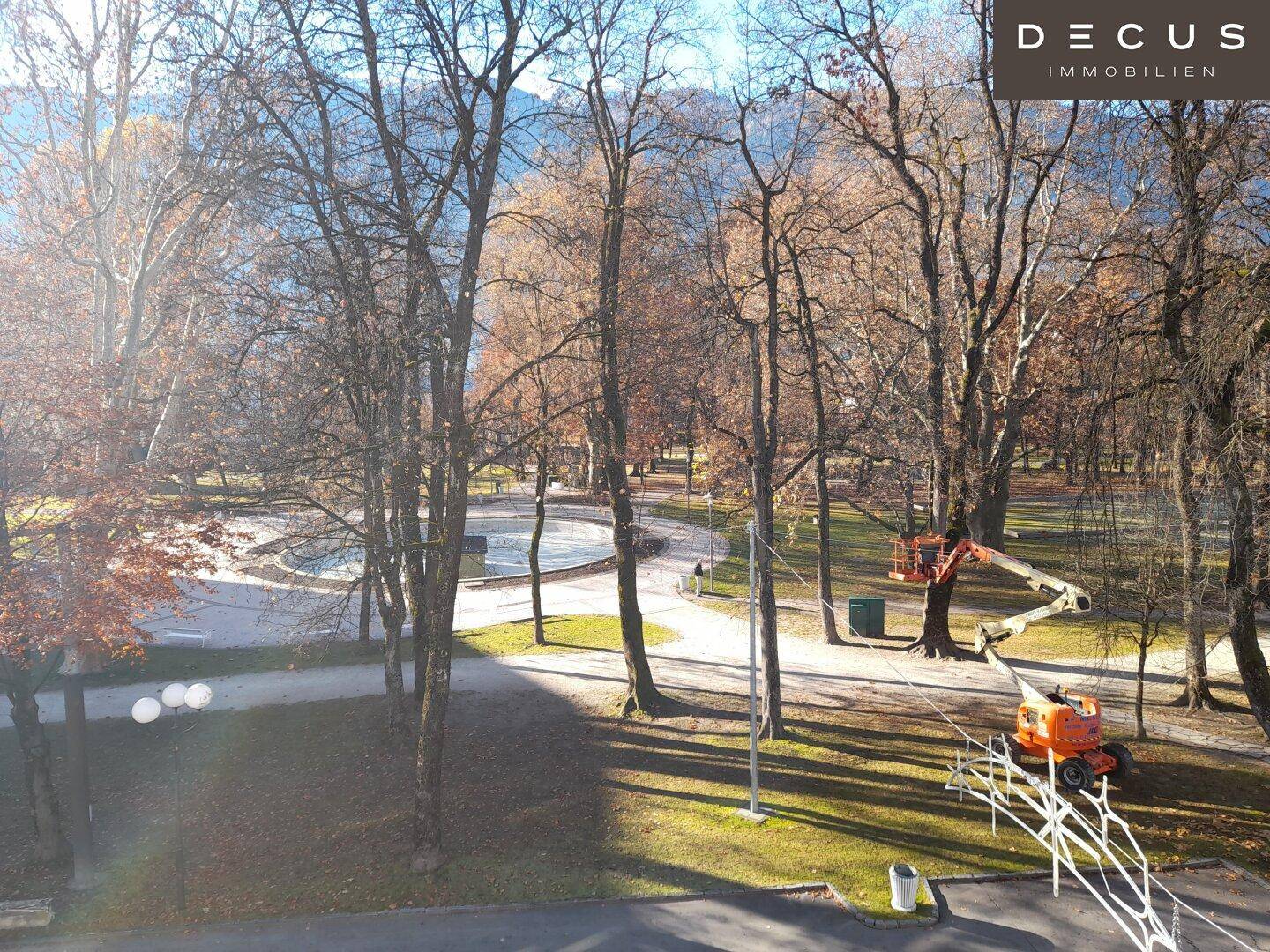 Weitläufiger Blick auf einen Stadtpark mit Bäumen und einem Teich an einem sonnigen Tag.
