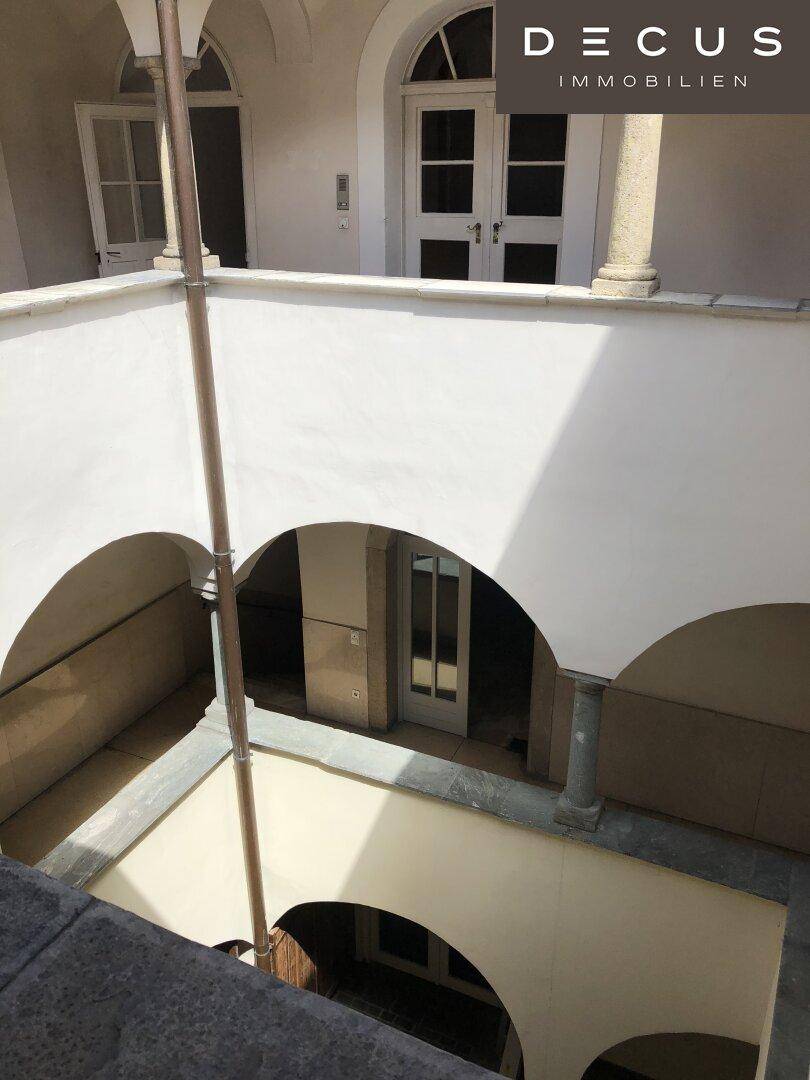 Blick von oben in einen hellen Innenhof mit Arkaden und Säulen, der viel Licht spendet.