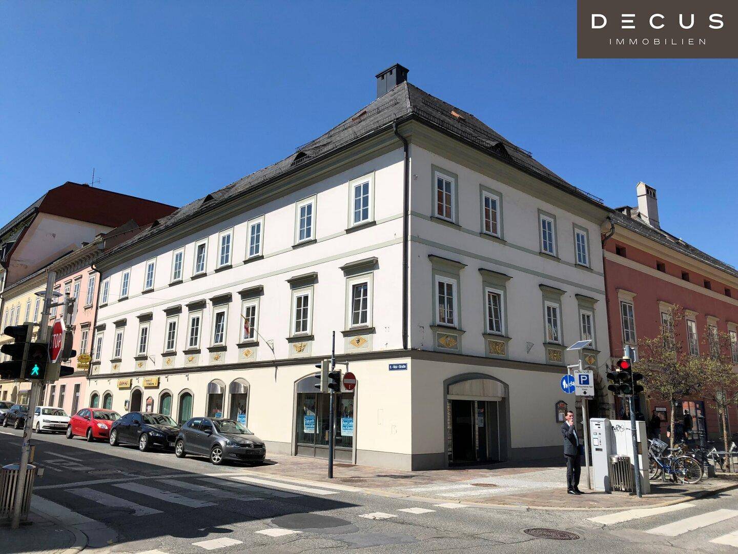 Historisches Eckgebäude an einer belebten Straße unter blauem Himmel, das viel Sonnenlicht erhält.