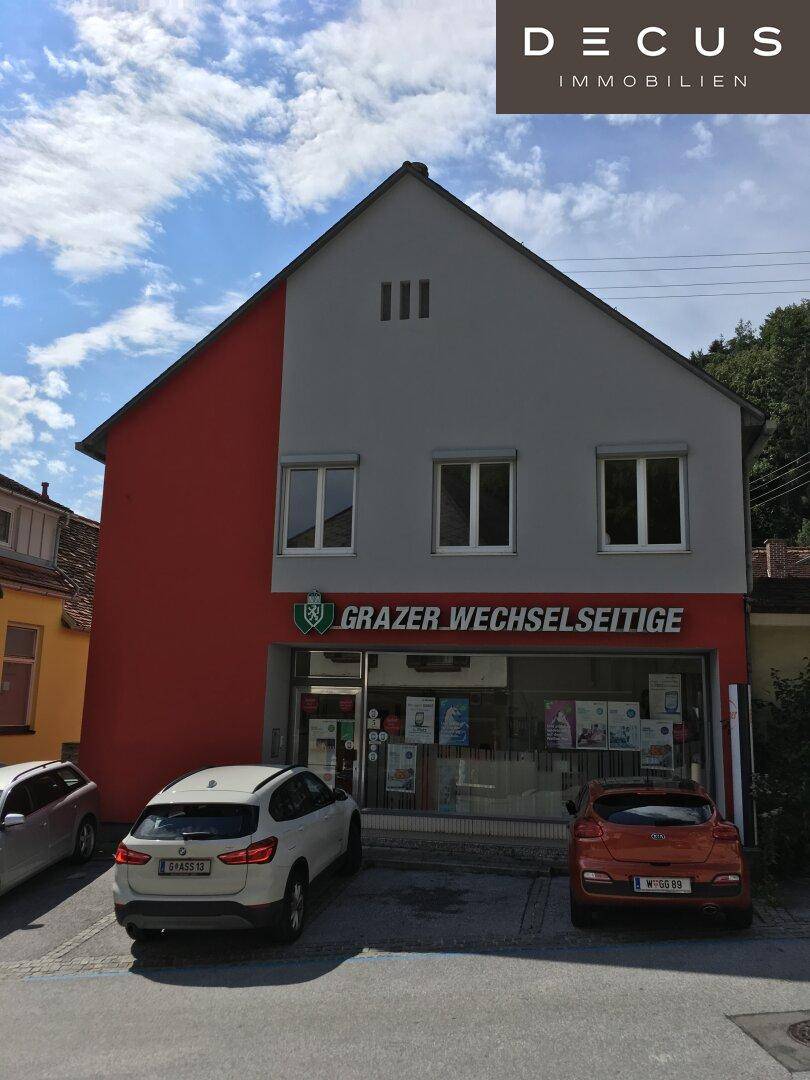 Vorderansicht des Gebäudes mit rot-grauer Fassade und geparkten Autos vor dem Geschäft.
