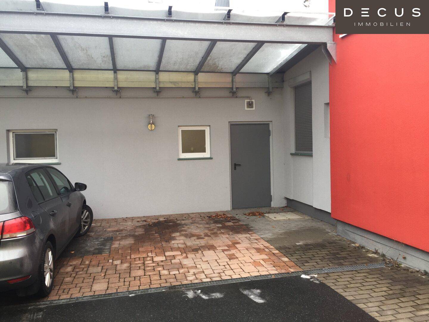 Detailansicht des überdachten Parkplatzes mit geparktem Auto und Seiteneingang.