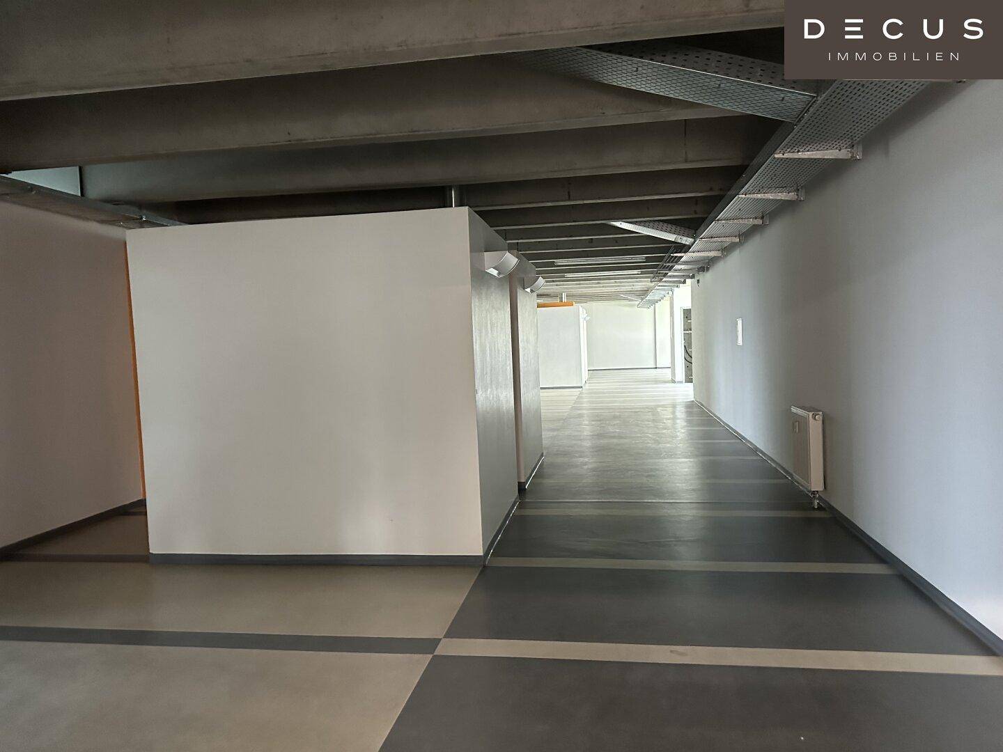 Langer, heller Flur mit sichtbaren Kabeltrassen und Heizkörpern, ideal für Büronutzung.