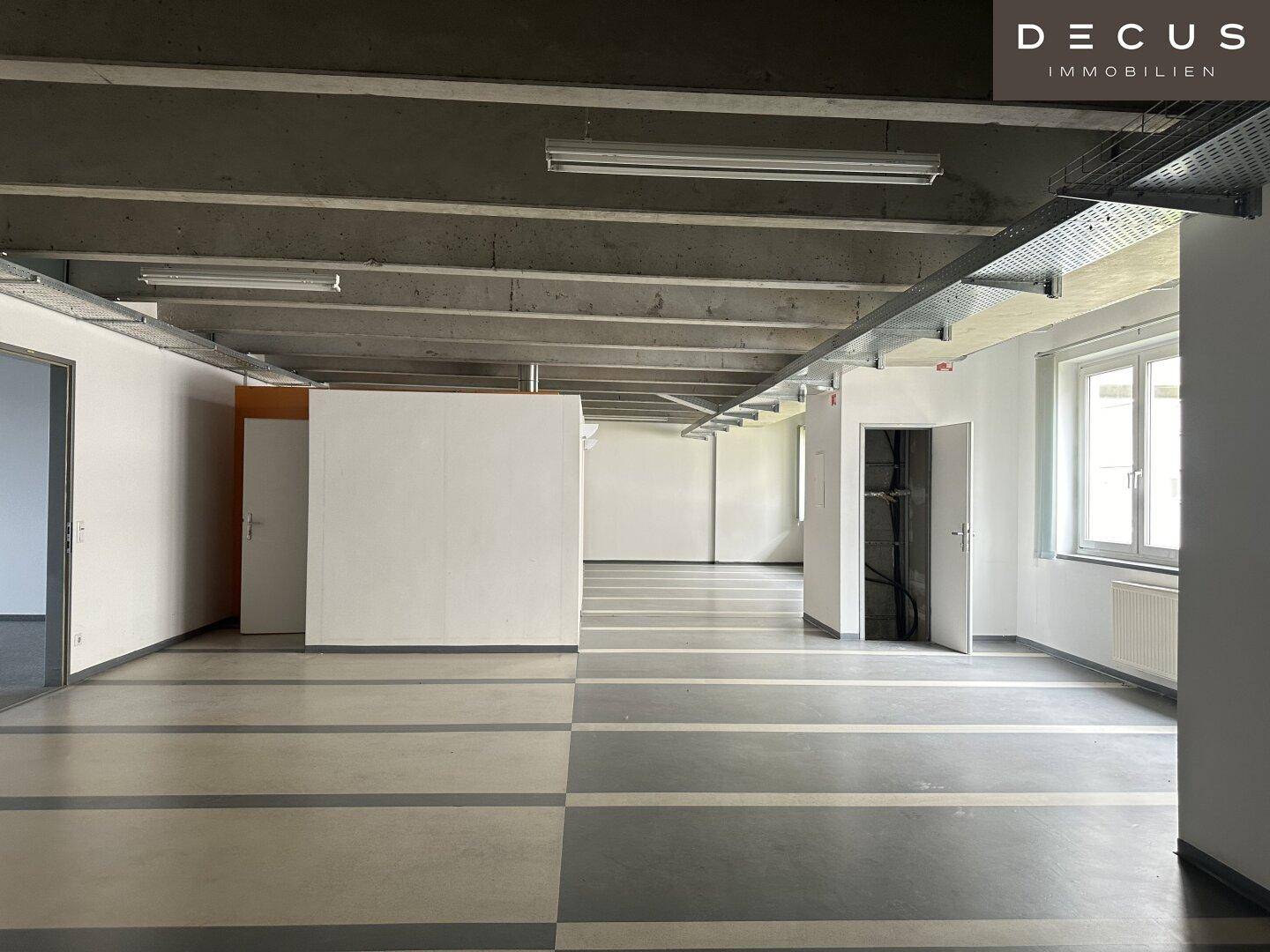 Großer, offener Bürobereich mit unterschiedlichen Bodenbelägen und viel Tageslicht.