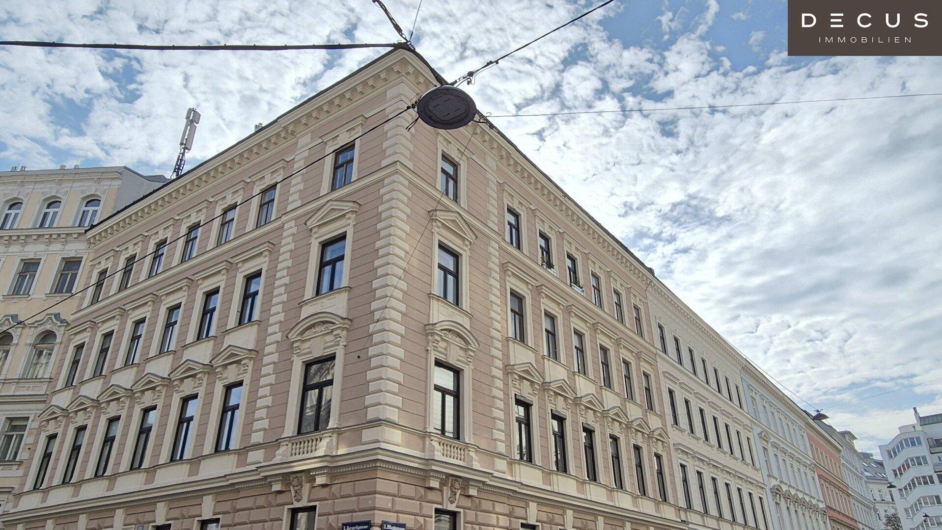 Elegantes Eckgebäude mit klassischer Architektur und vielen Fenstern unter bewölktem Himmel.