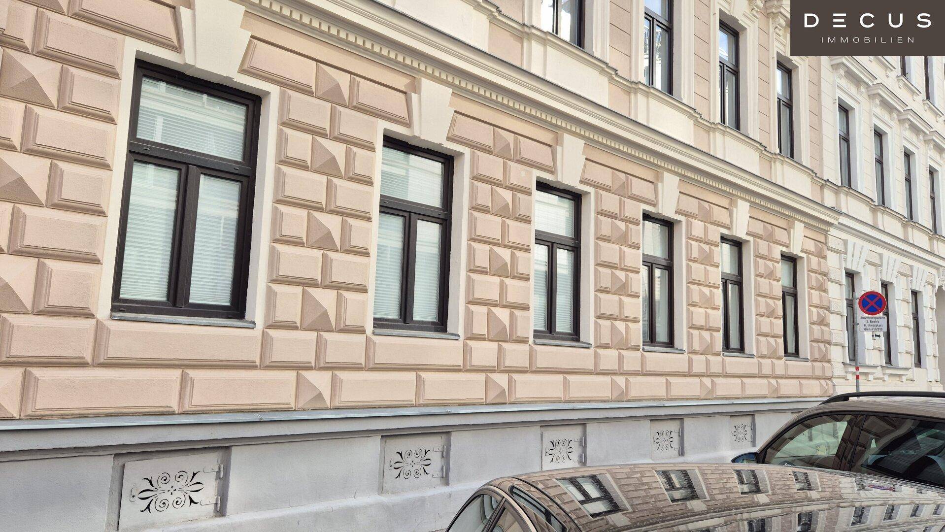 Fassade eines historischen Gebäudes mit verzierten Fenstern und geparkten Autos entlang der Straße.