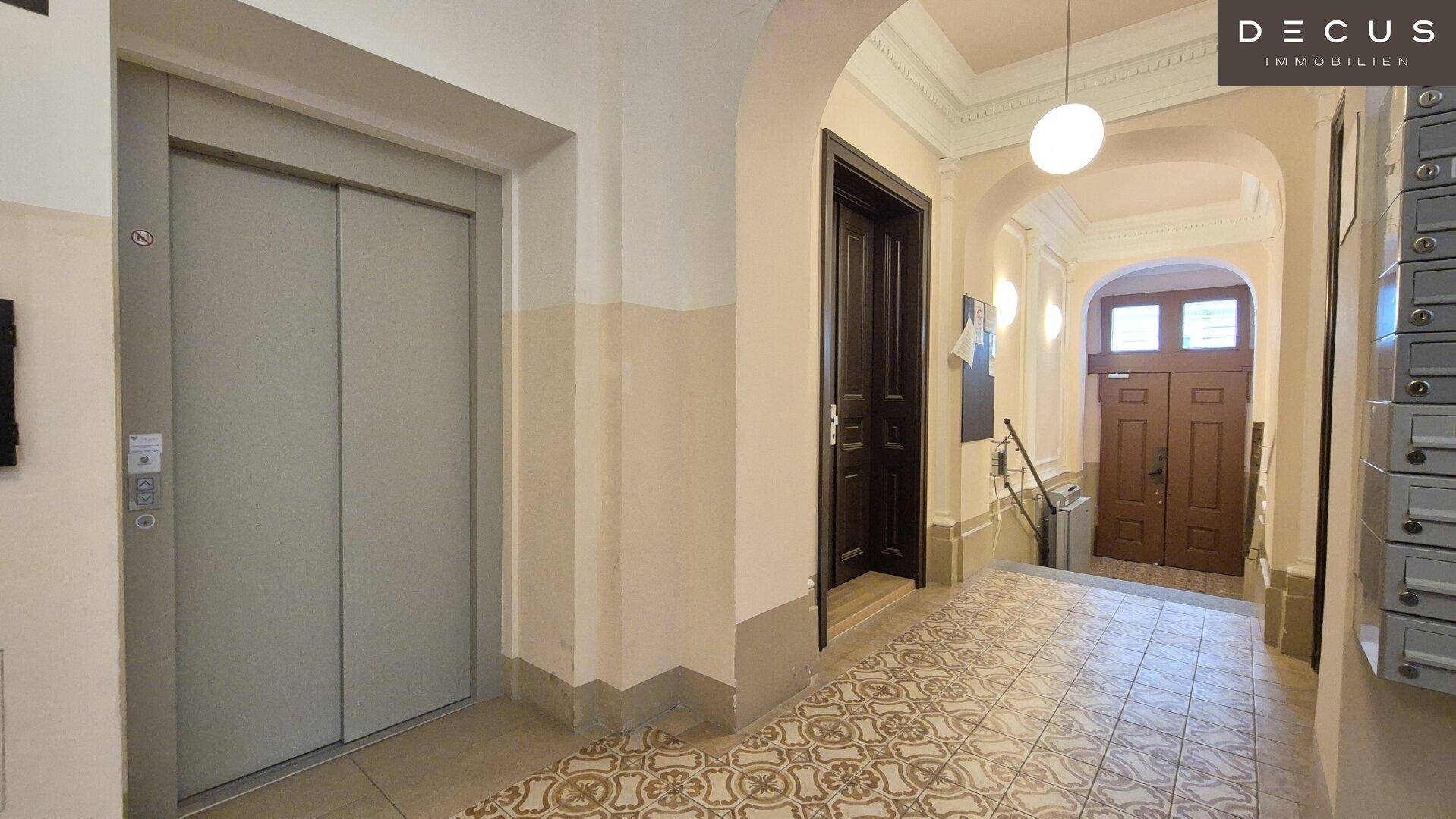 Heller Eingangsbereich mit Aufzug, gemustertem Fliesenboden und hohen Decken in einem Altbau.