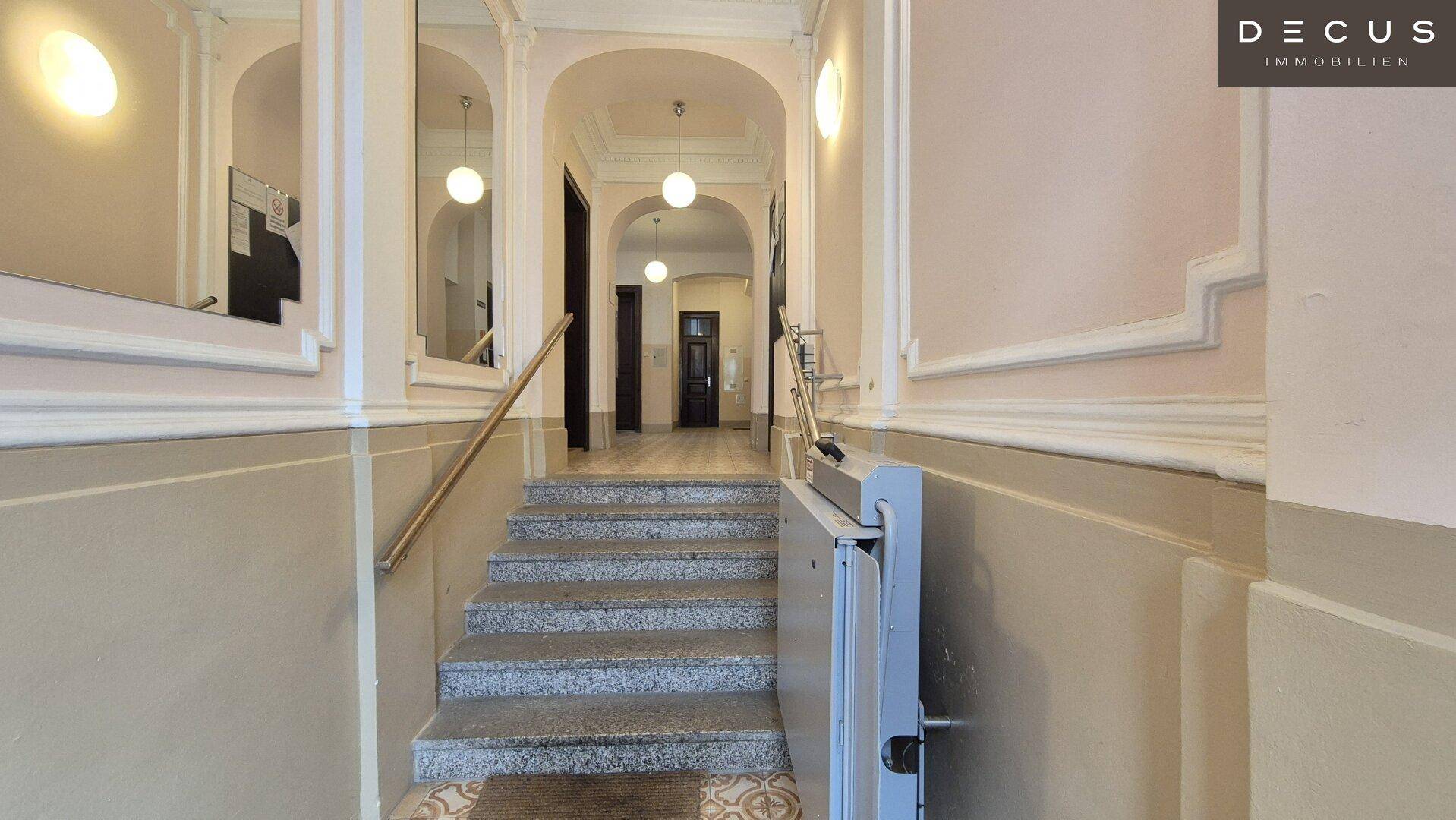 Historisches Treppenhaus mit Marmorstufen, schmiedeeisernem Geländer und einem Treppenlift für Barrierefreiheit.