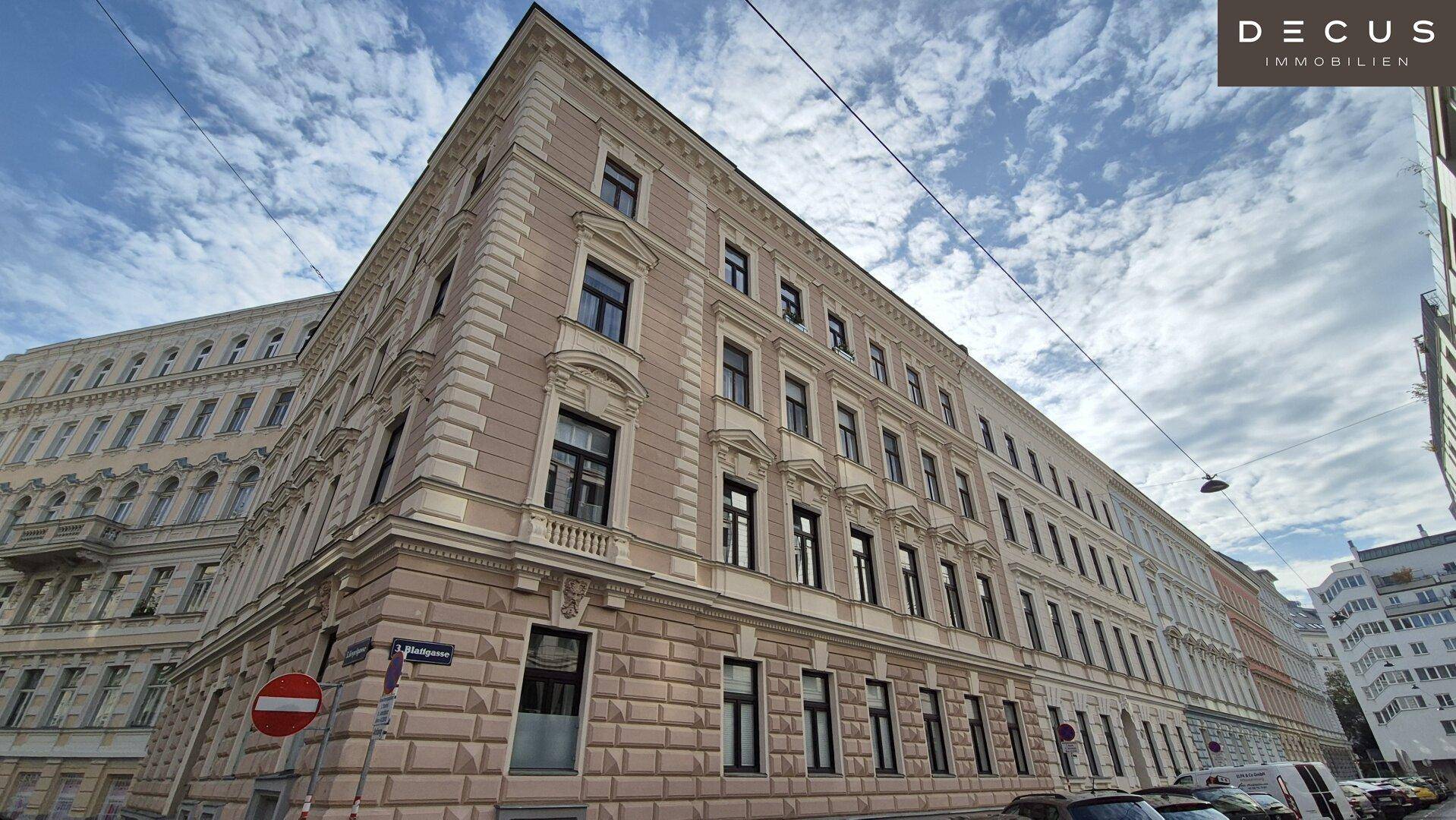 Elegantes Eckgebäude mit klassischer Architektur und vielen Fenstern unter bewölktem Himmel.