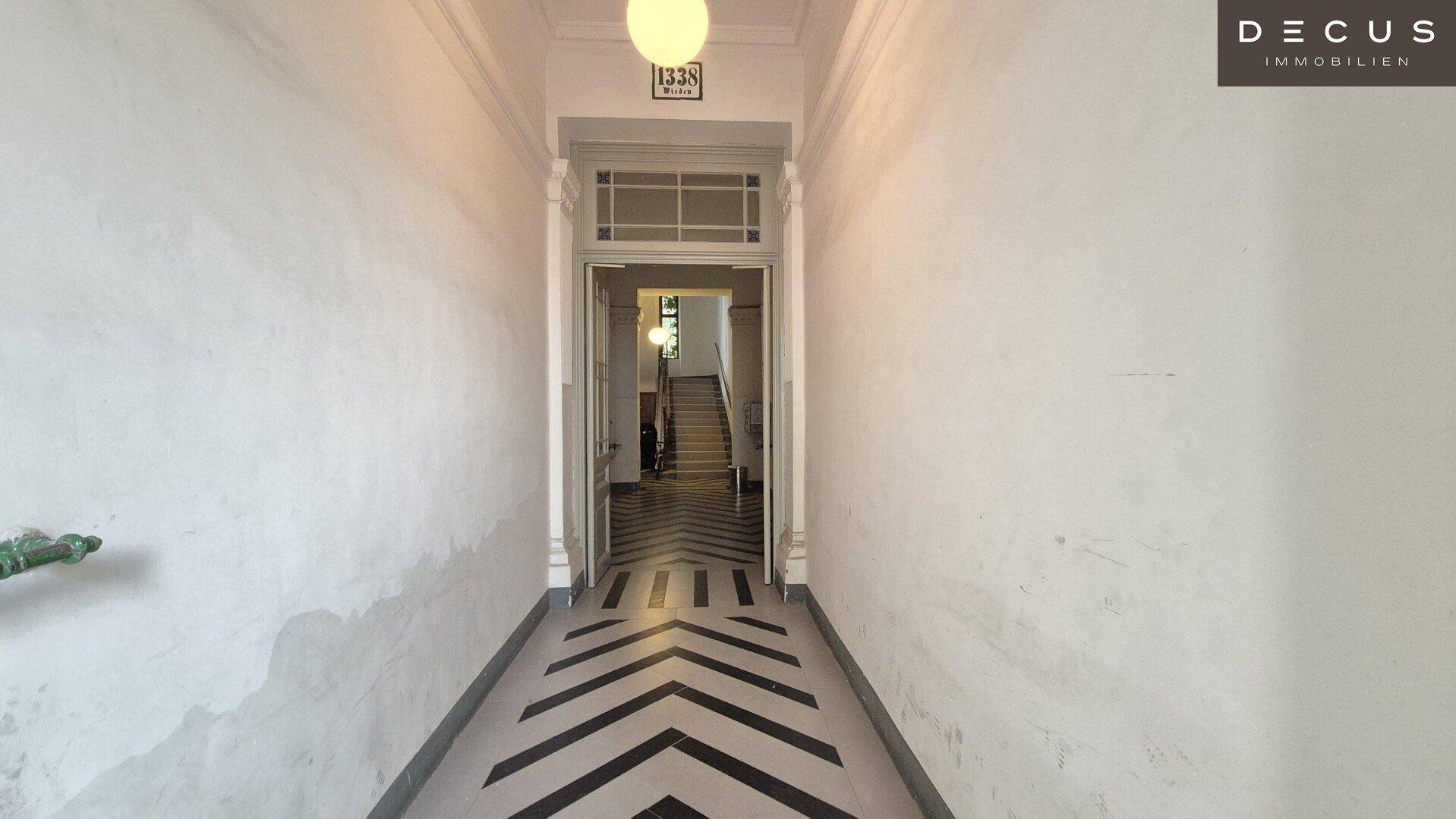 Langer Eingangsbereich eines Altbaus mit markantem schwarz-weißem Fliesenboden und hoher Decke.