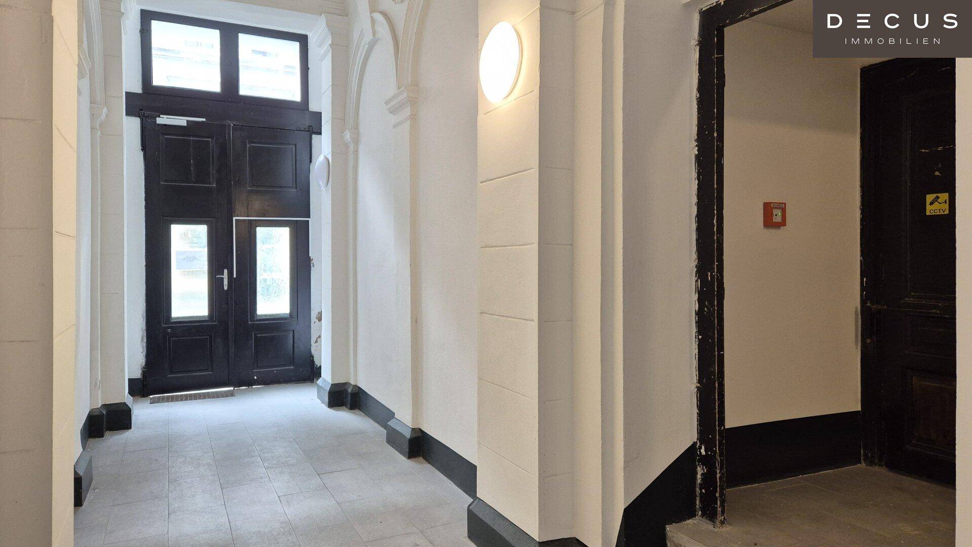 Eingangsbereich des Gebäudes mit großen Holztüren und klassischer Architektur, gut beleuchtet.