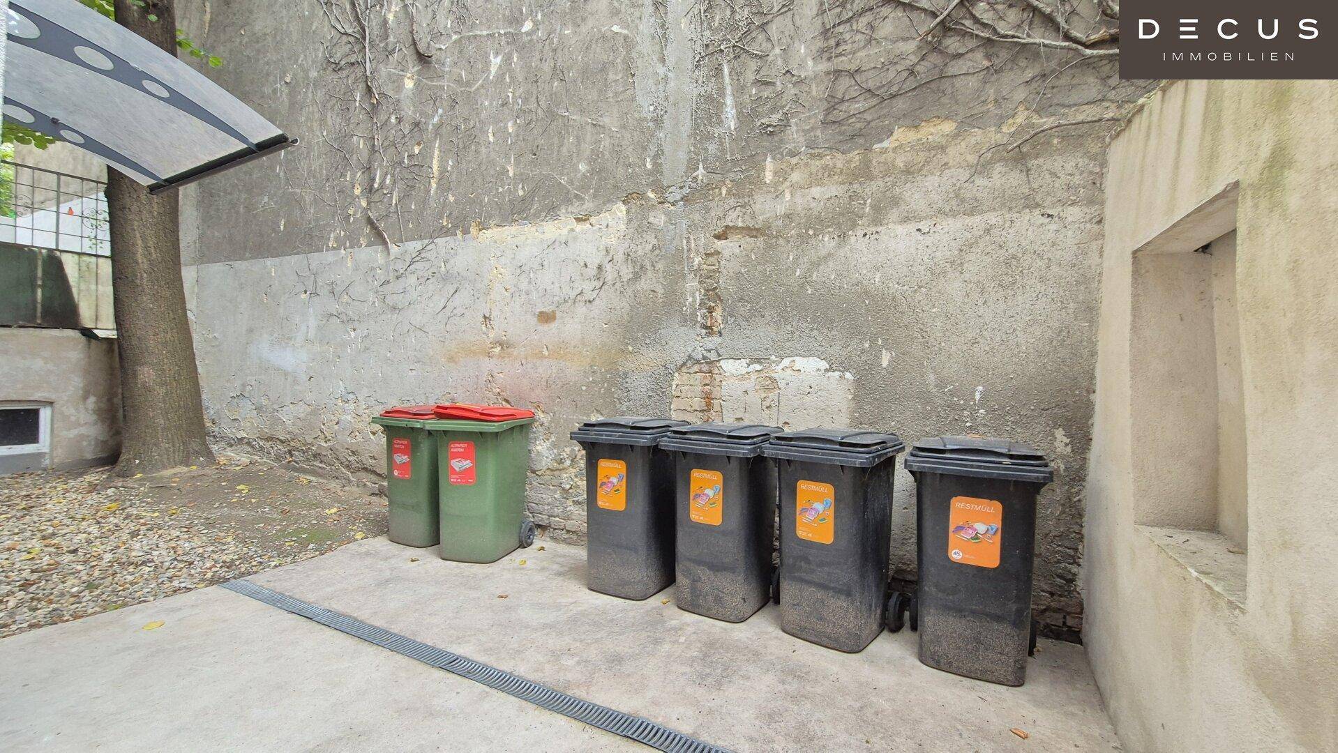 Hinterhofbereich mit Mülltonnen und einer schlichten Betonwand, zweckmäßig gestaltet.