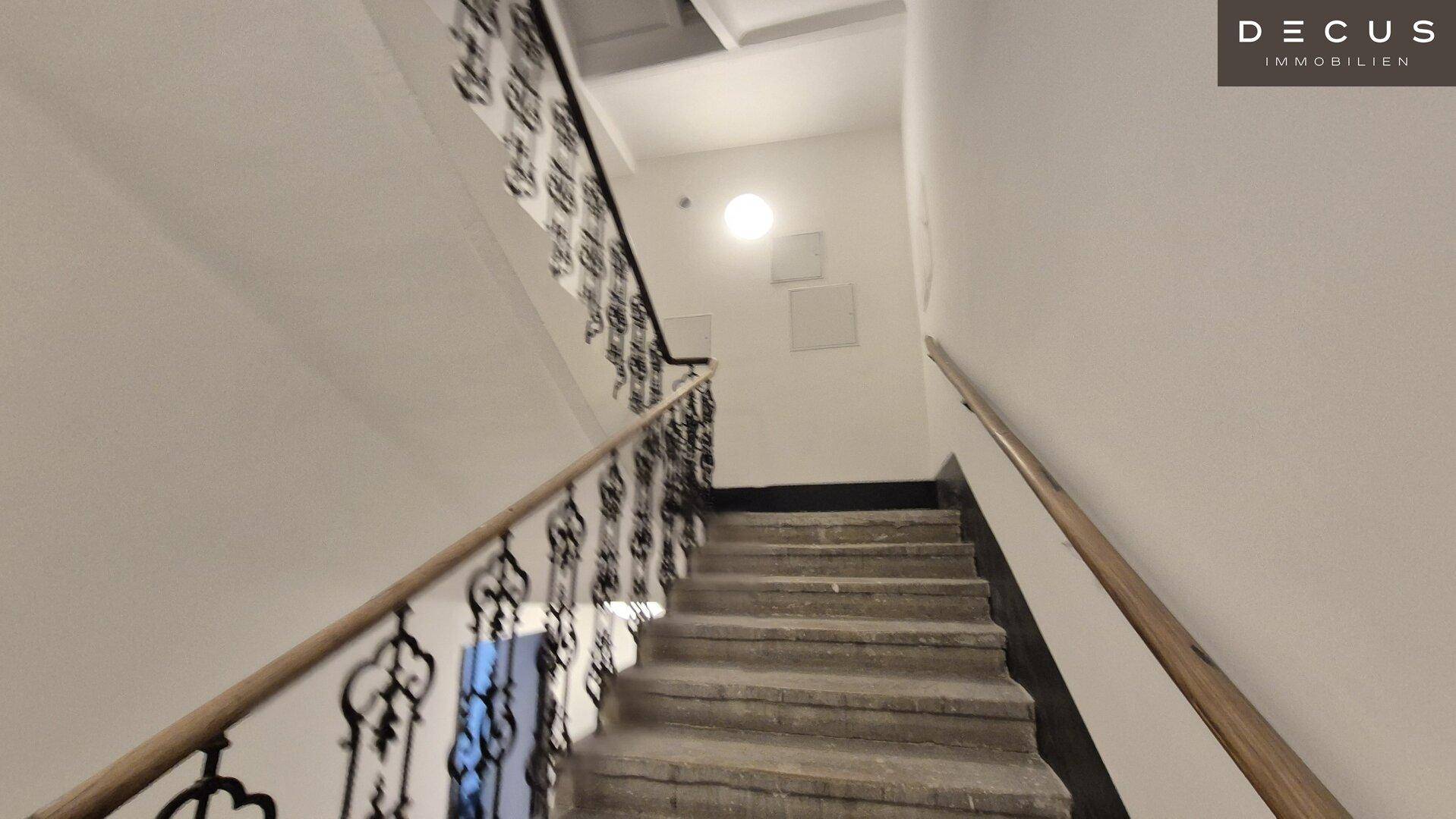 Historisches Treppenhaus mit schmiedeeisernem Geländer und Steinstufen, das in die oberen Etagen führt.
