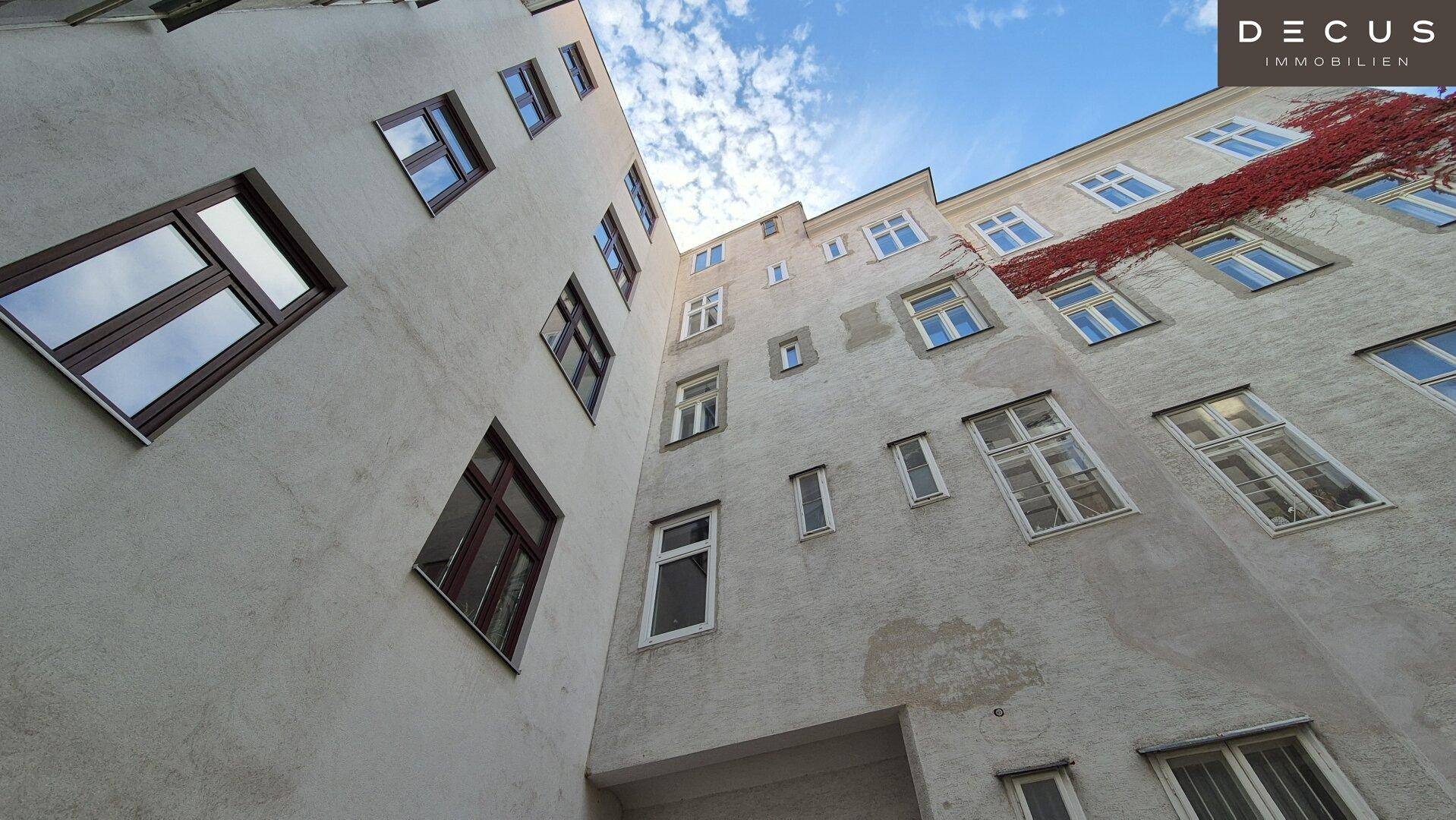 Innenhofansicht des Gebäudes mit verschiedenen Fenstern und einer bewachsenen Wand unter blauem Himmel.