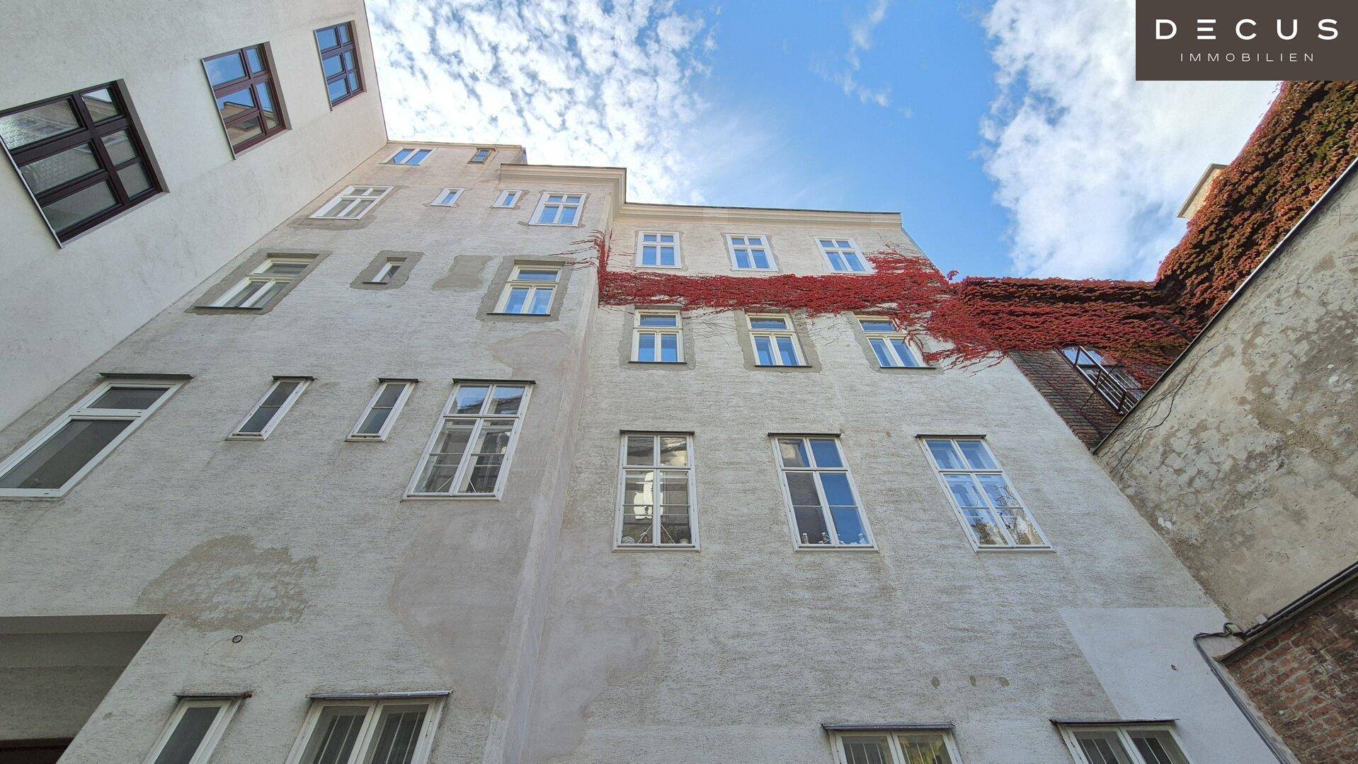 Blick in den Innenhof des Gebäudes mit unregelmäßigen Fenstern und einer roten Kletterpflanze an der Fassade.