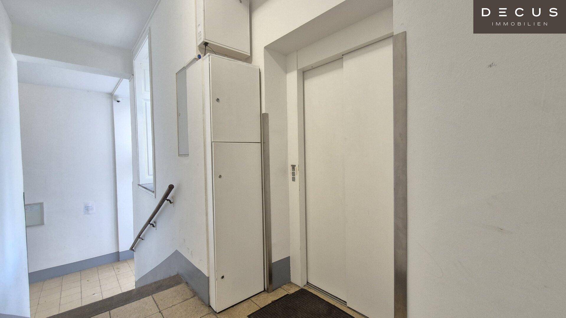 Treppenhaus mit Aufzug und schlichten Wänden, typisch für ein älteres Wohngebäude.