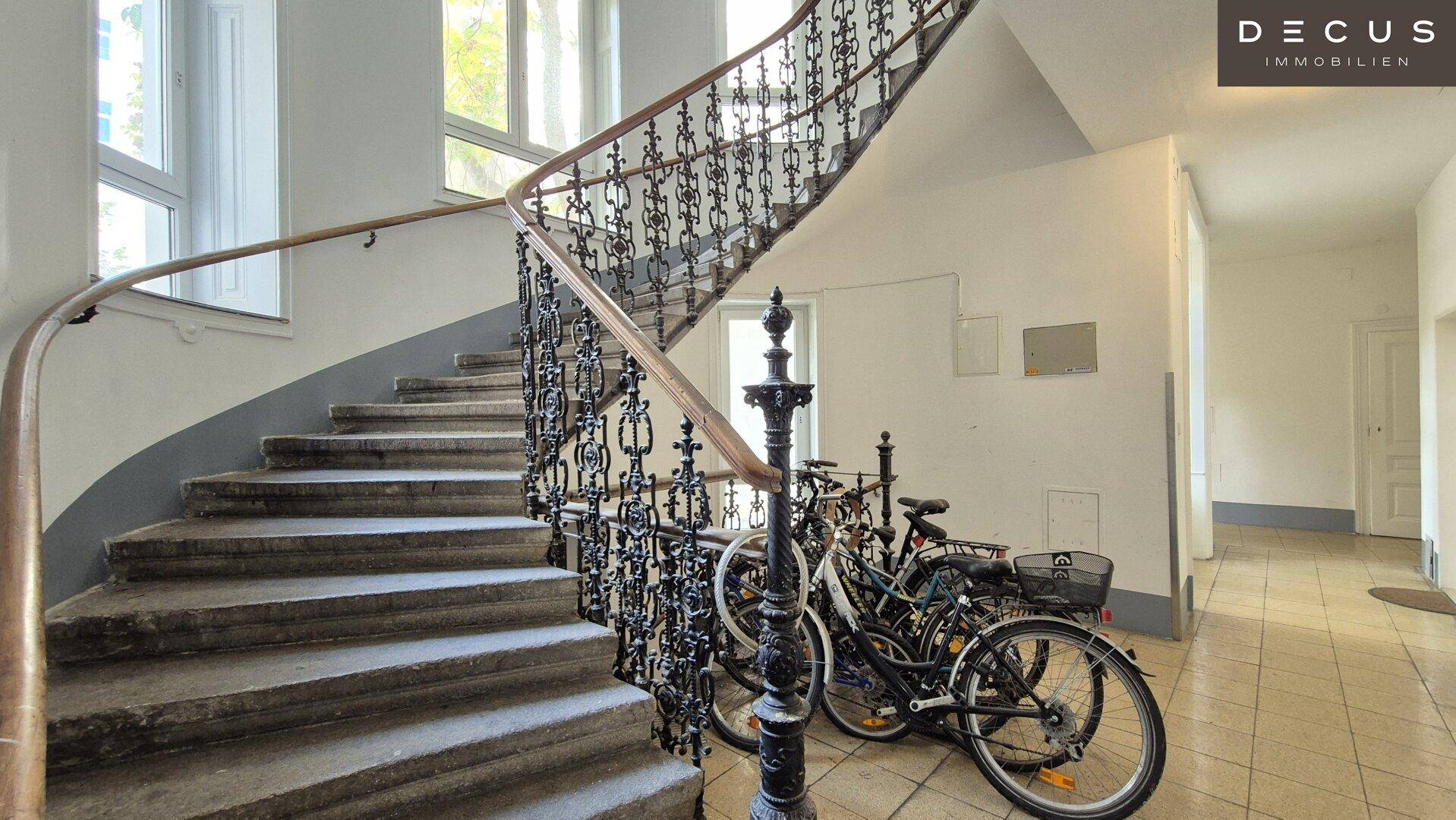 Historisches Treppenhaus mit schmiedeeisernem Geländer und Fahrrädern im Eingangsbereich.