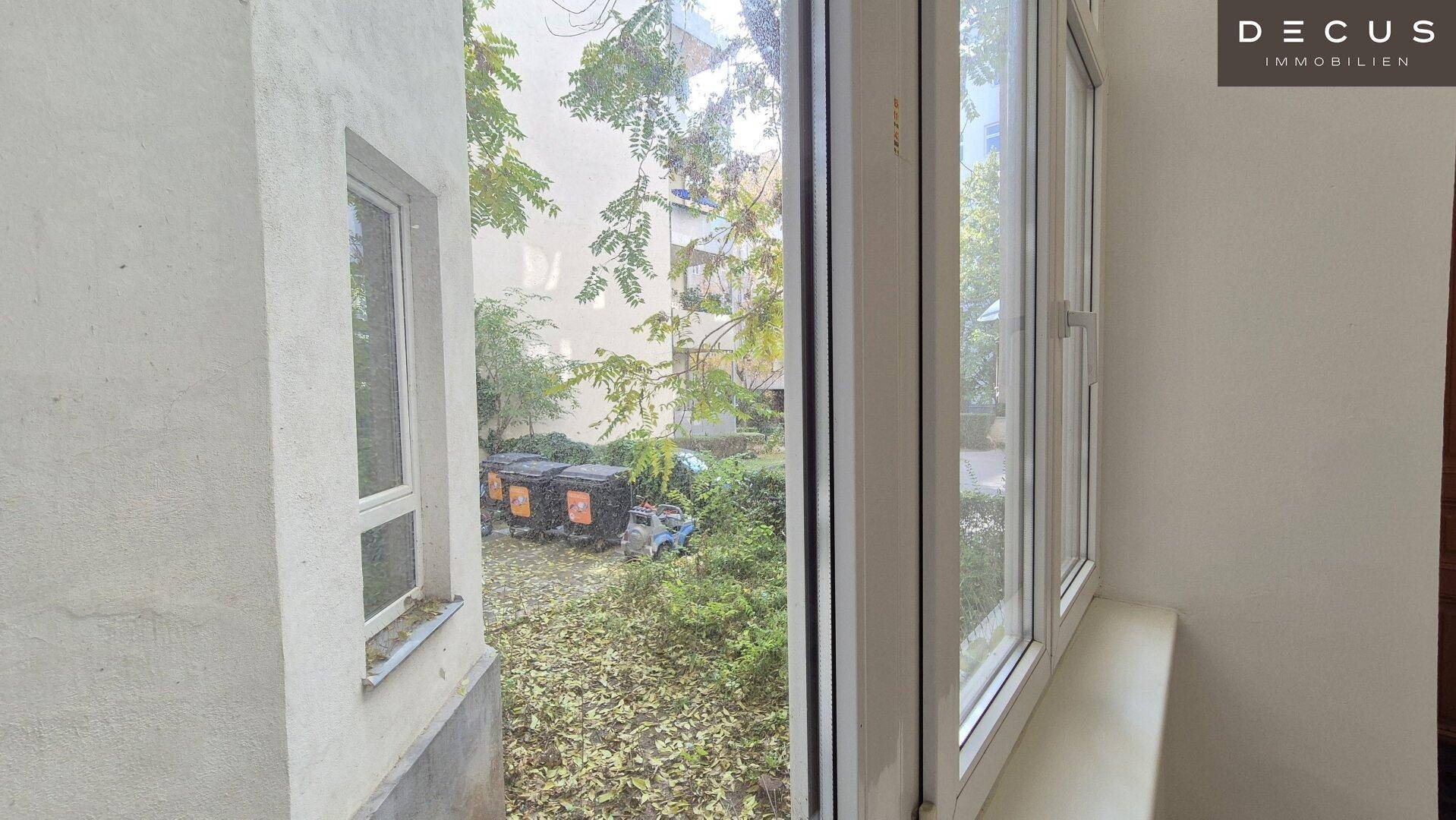Blick aus einem Fenster in einen begrünten Innenhof mit Mülltonnen und Bäumen.