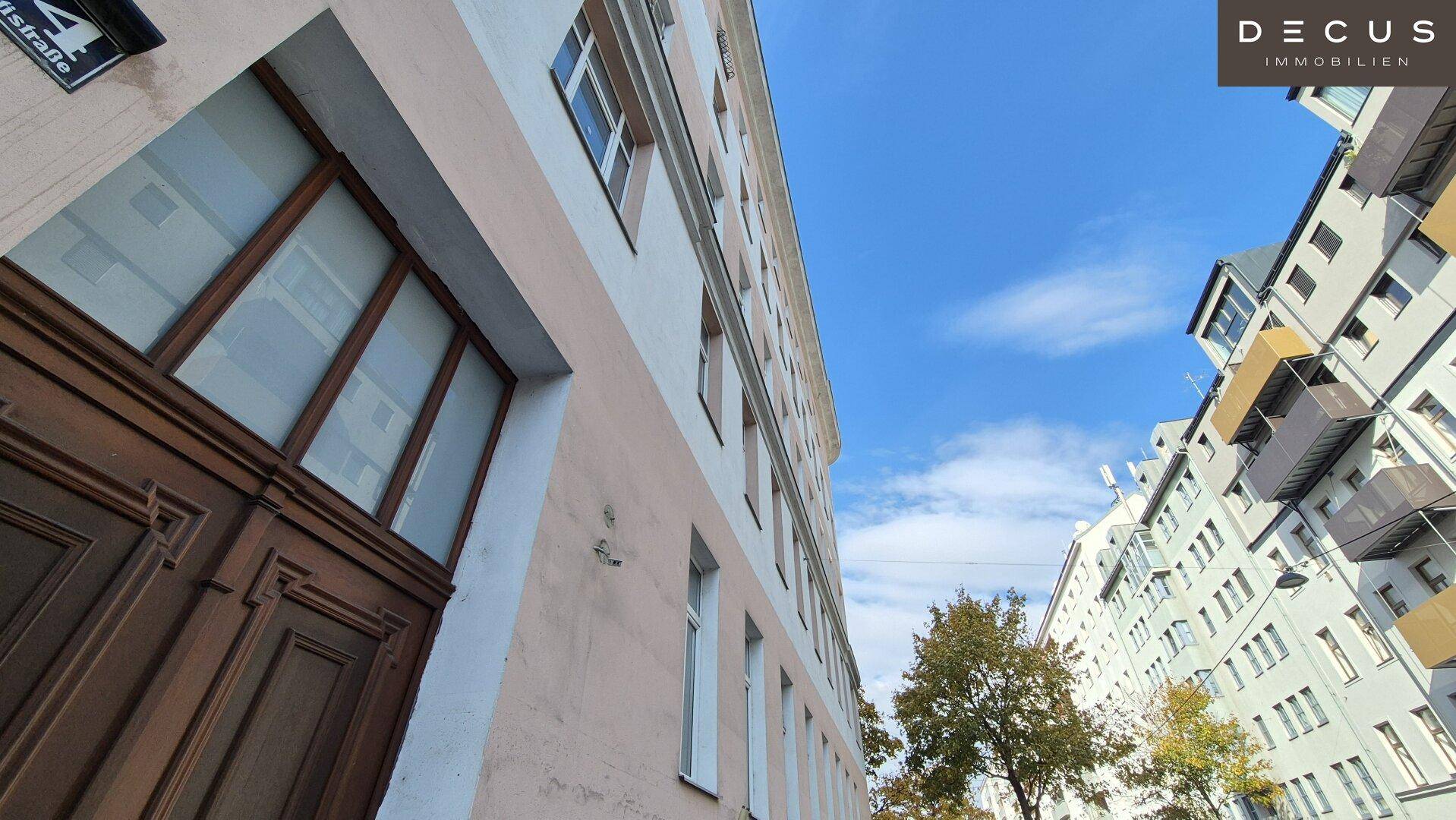 Eingangsbereich eines Altbaus mit Holztür und Blick auf die Fassade und den blauen Himmel.