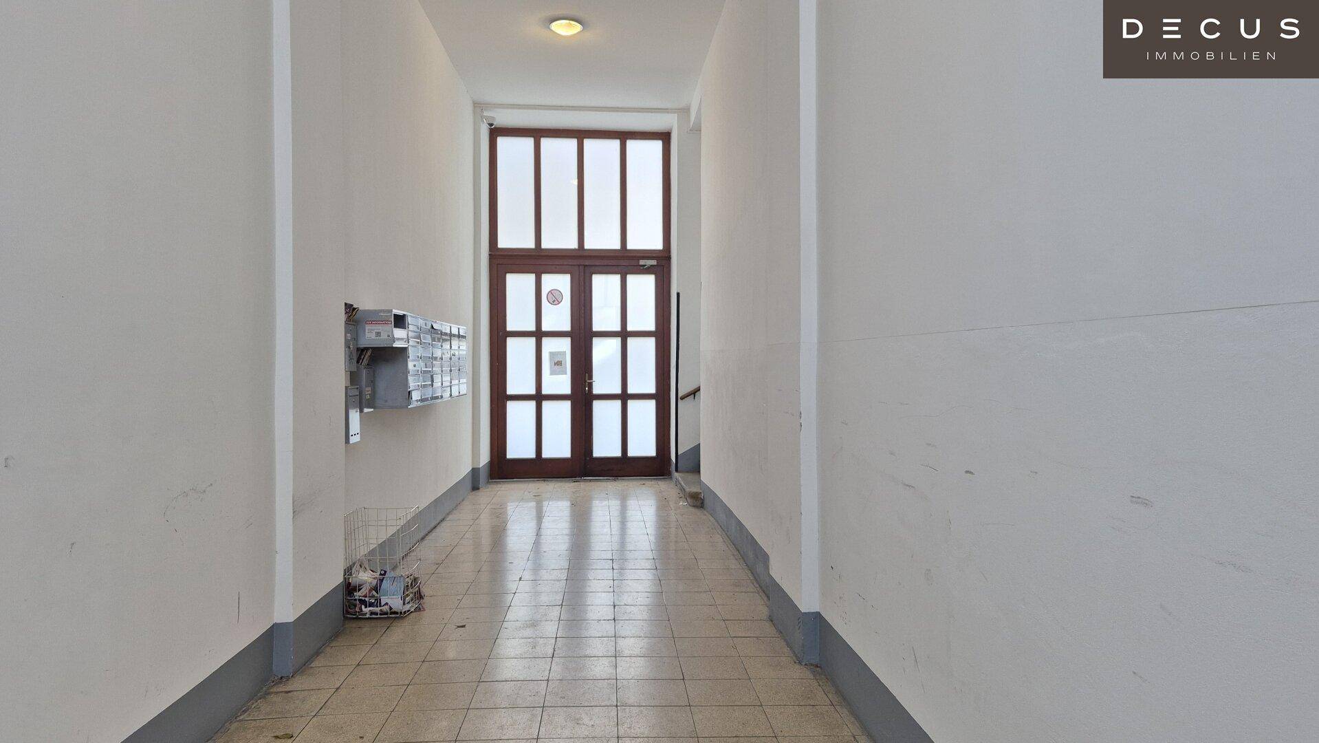 Langer Eingangsbereich mit Fliesenboden, Briefkästen an der Wand und einer großen Holztür.