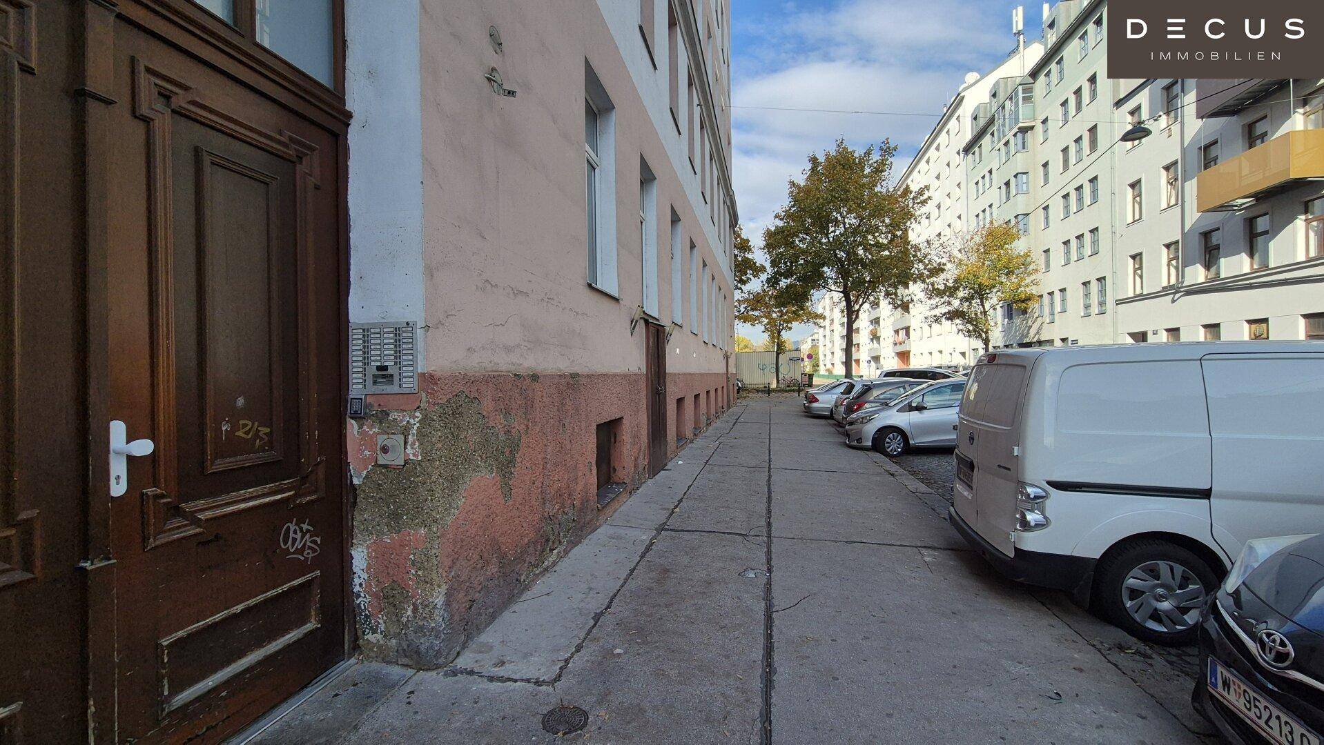 Seitenansicht des Gebäudes mit abgenutzter Fassade und geparkten Autos entlang der Straße.