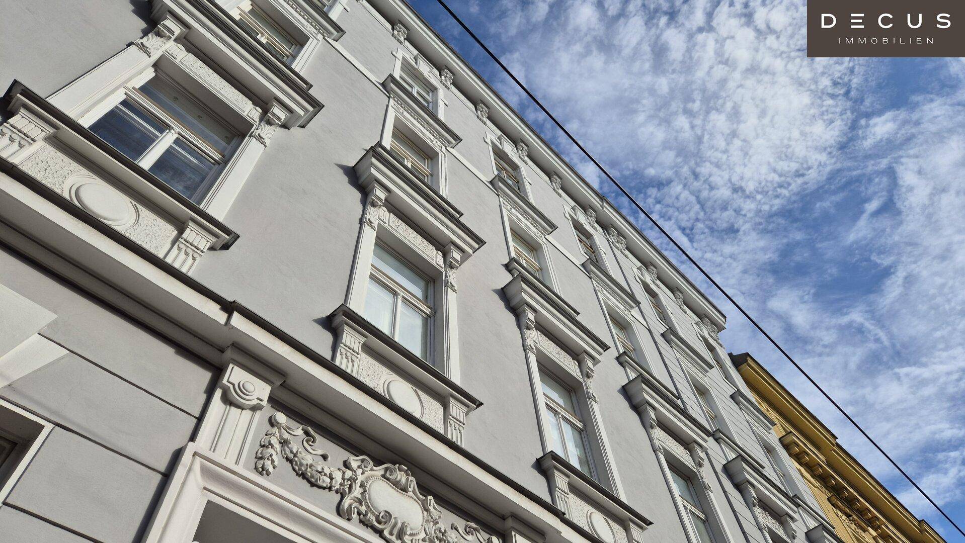 Detailansicht der historischen Fassade mit verzierten Fenstern und Stuckelementen unter blauem Himmel.