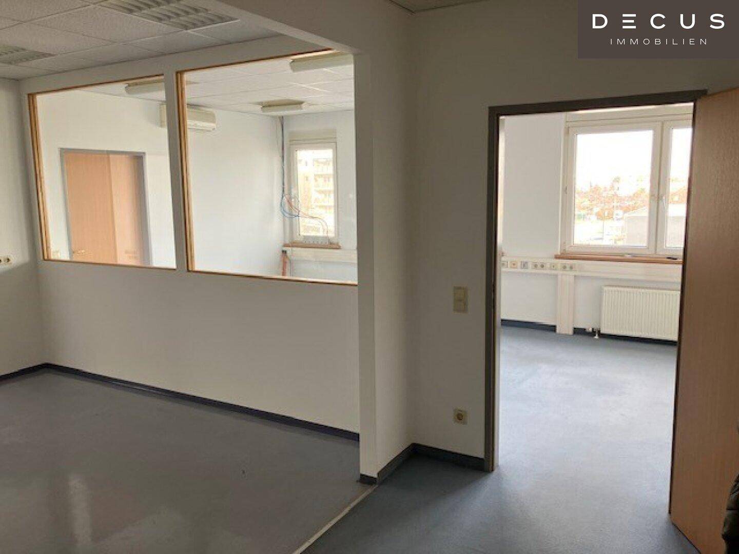 Büro mit Trennwänden aus Glas und Holzrahmen, Blick auf Fenster, Heizkörper und die Umgebung.