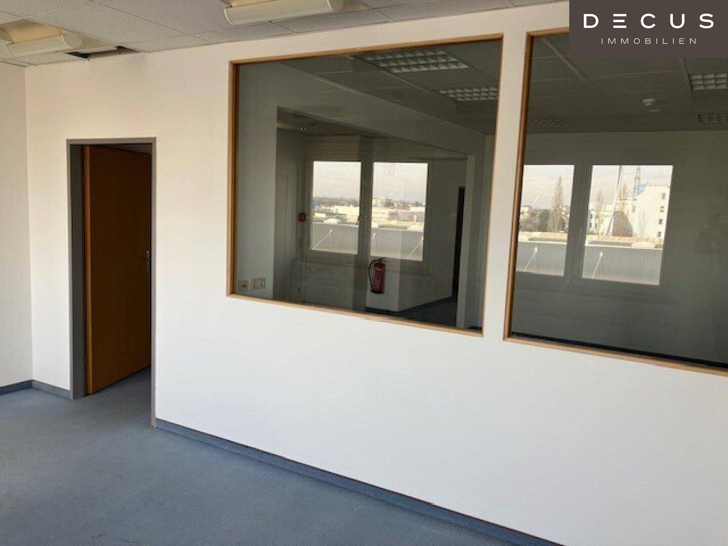 Büro mit Glaswänden, die einen Blick in den Nebenraum und auf die Außenansicht ermöglichen.