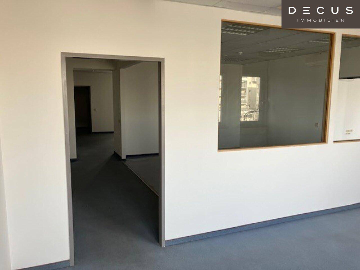 Flur in einem Bürogebäude mit hellgrauem Vinylboden und Blick in angrenzende Büroräume.
