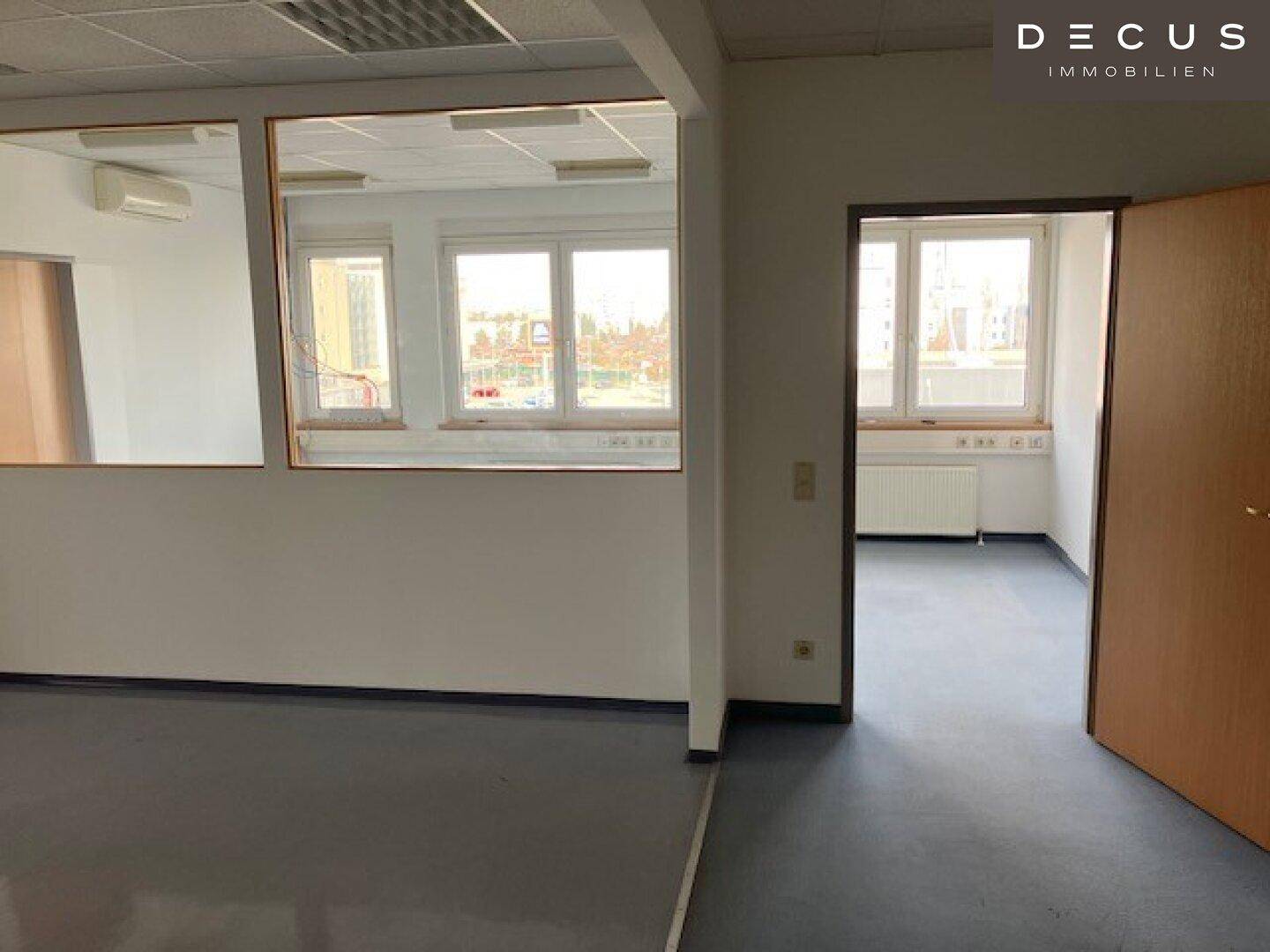 Büro mit Glaswänden und Blick in einen weiteren Raum mit Fenstern und Heizkörpern.