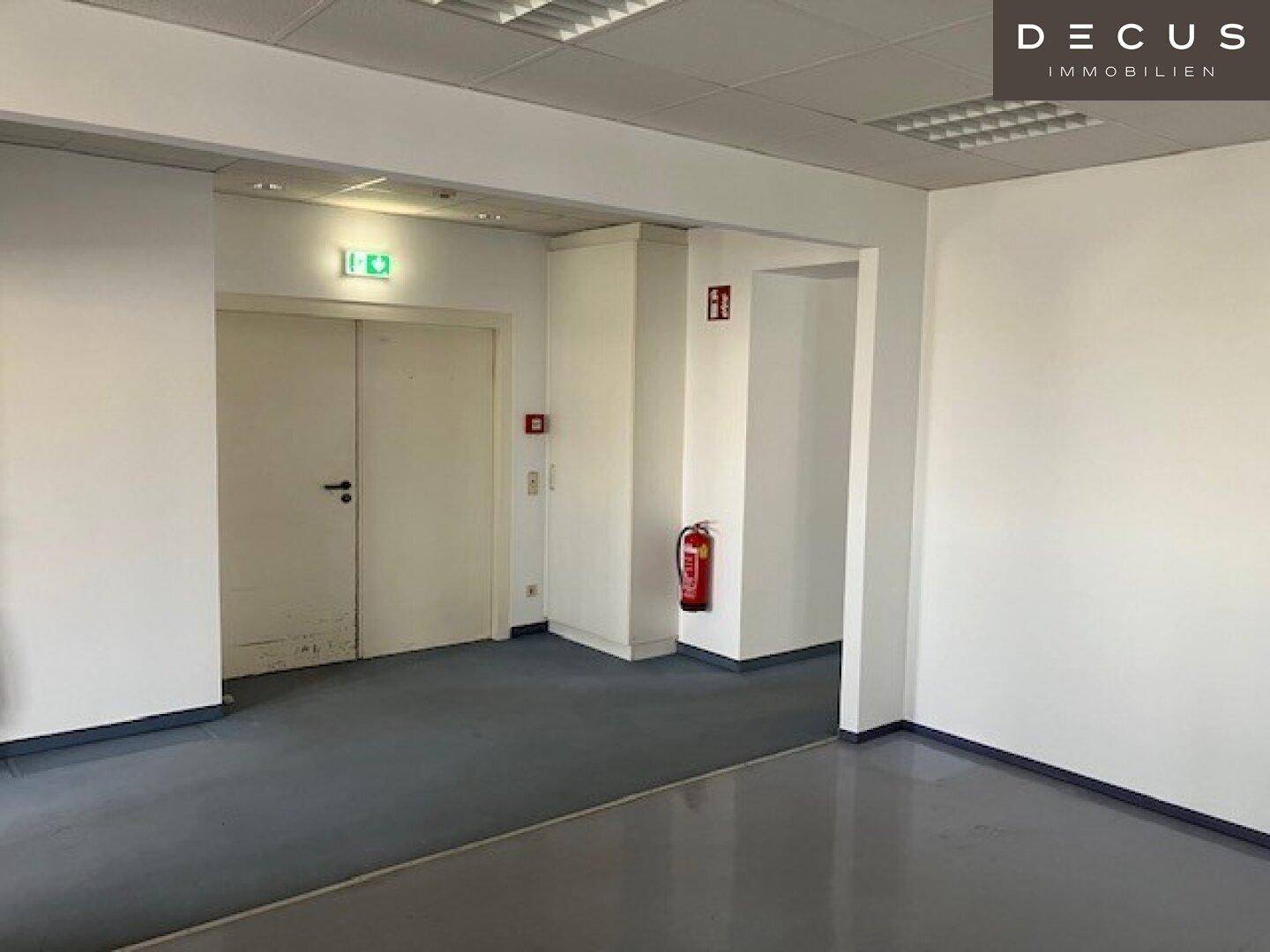 Flur mit zwei Türen, Feuerlöscher und hellgrauem Vinylboden in einem Bürogebäude.