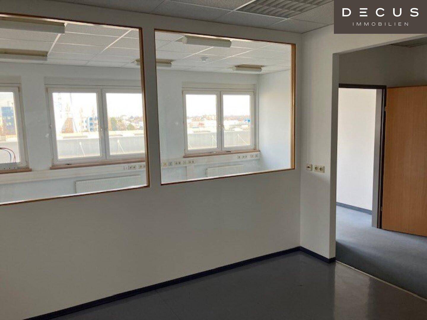 Büro mit Glaswänden, die einen Blick in den Nebenraum und auf die Außenansicht ermöglichen.