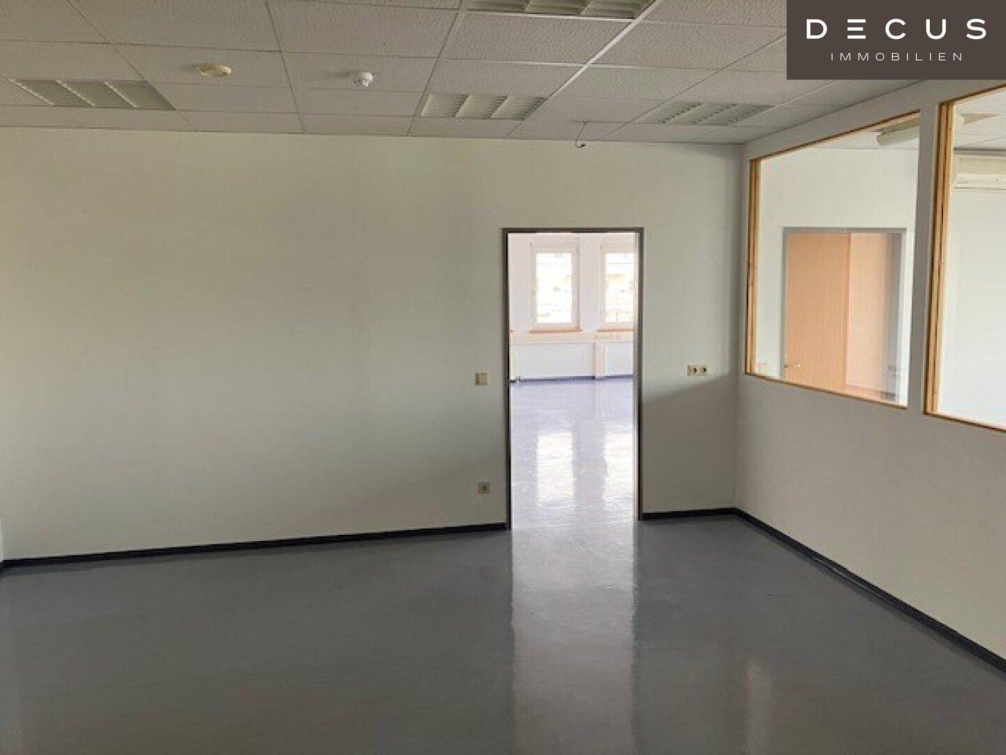 Leeres Büro mit hellgrauem Vinylboden, weißen Wänden und Blick in einen weiteren Raum.